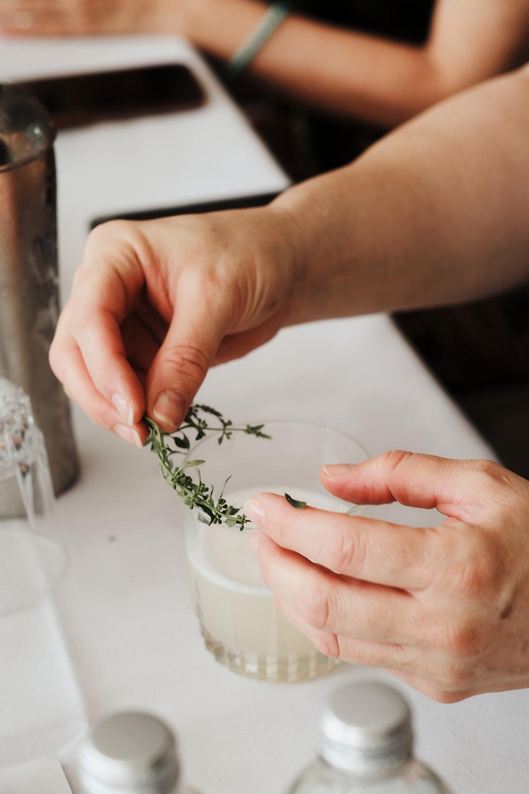 Hands sprinkling a herb garnish into a mocktail glass