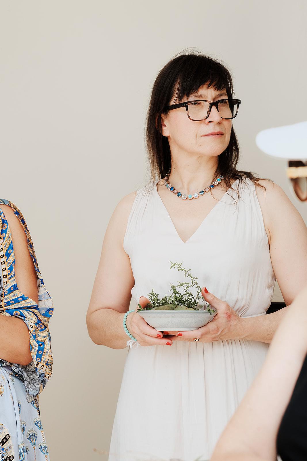 A woman holding a small bowl of foraged herbs indoors