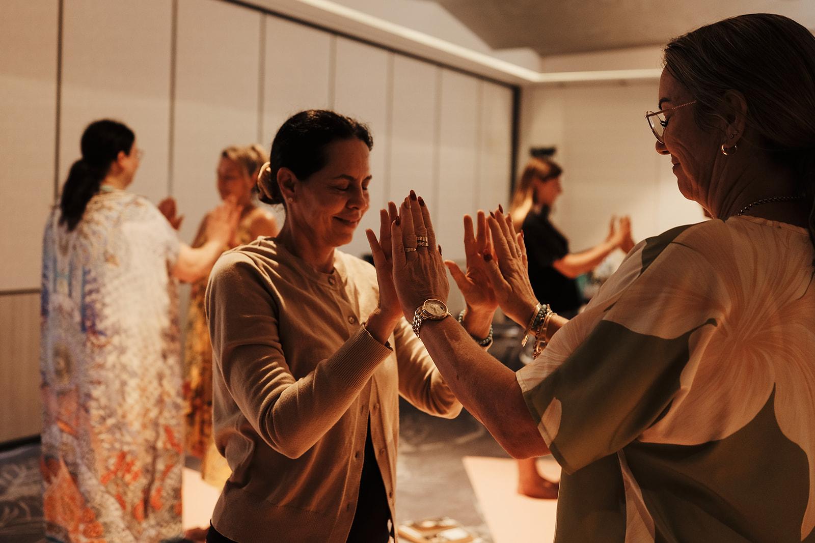 Pairs of women mirroring palms together with eyes closed, a group connection exercise