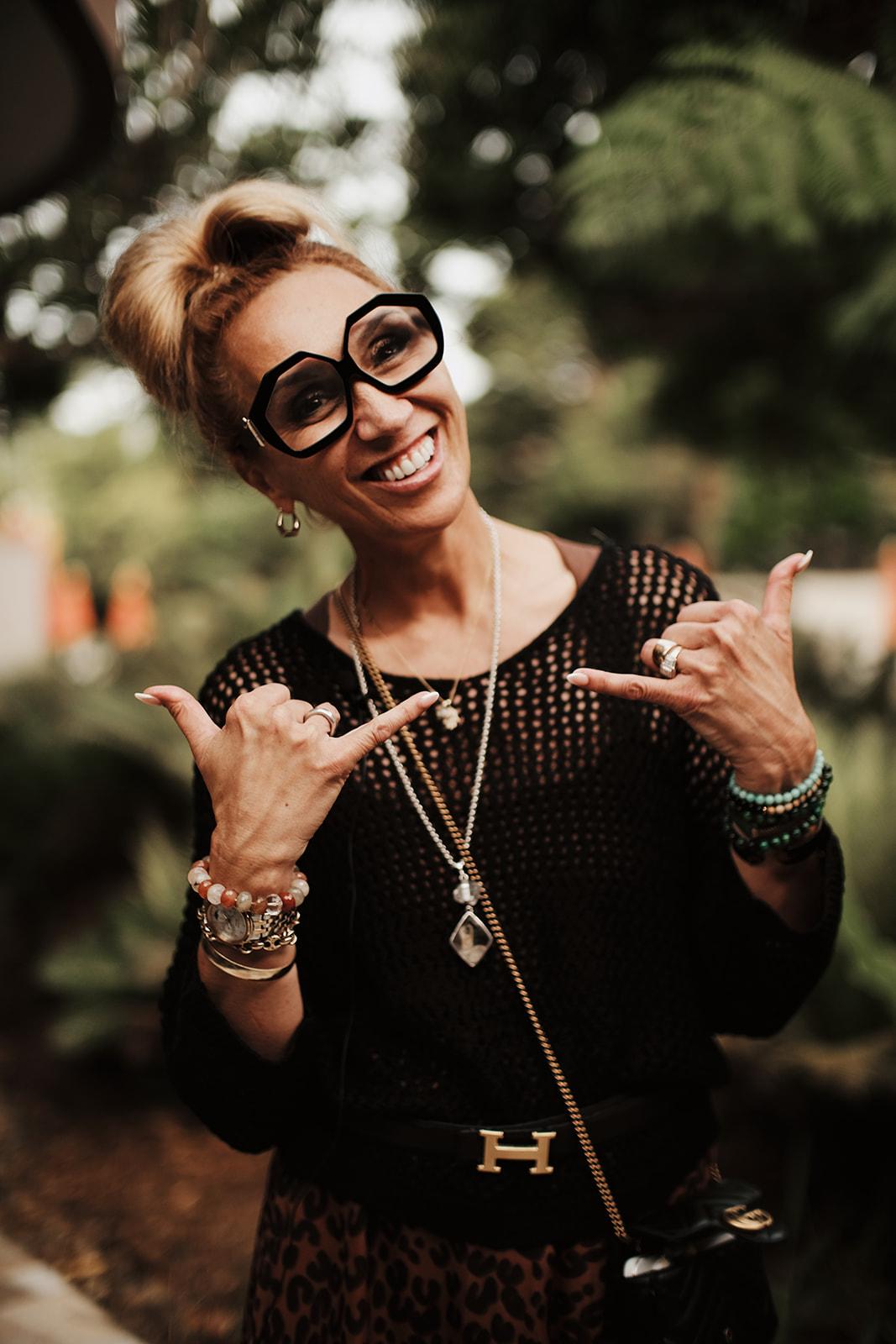 Portrait of a woman from the retreat, sunglasses on, hand raised in a playful gesture