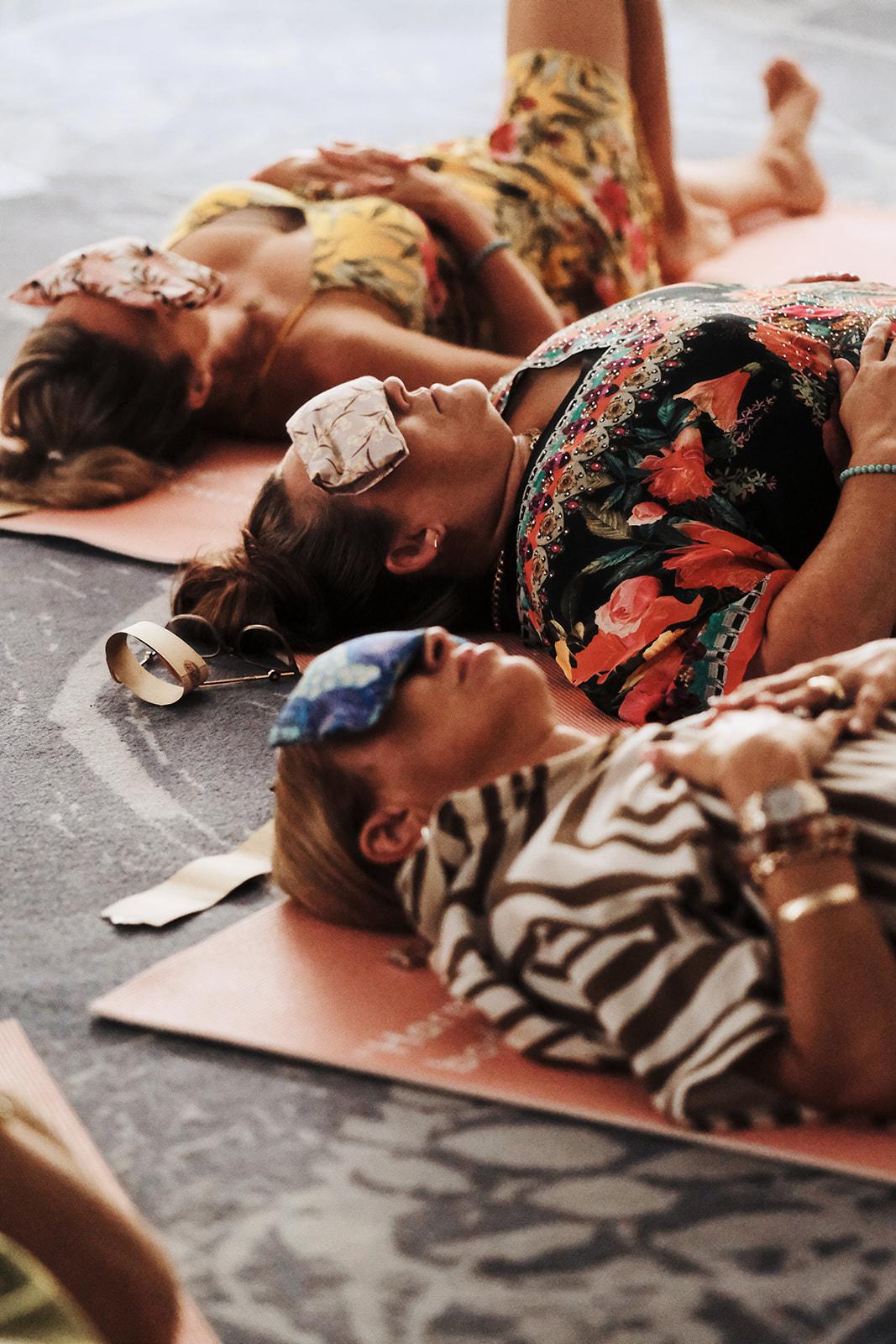 Two women lying on yoga mats outdoors, resting between sessions