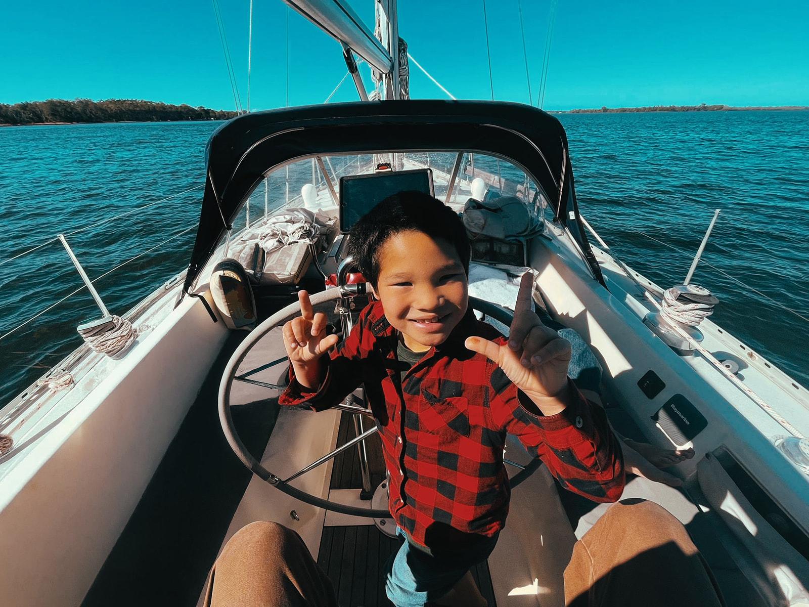 Koa at the helm, throwing up peace signs, sailing on open water