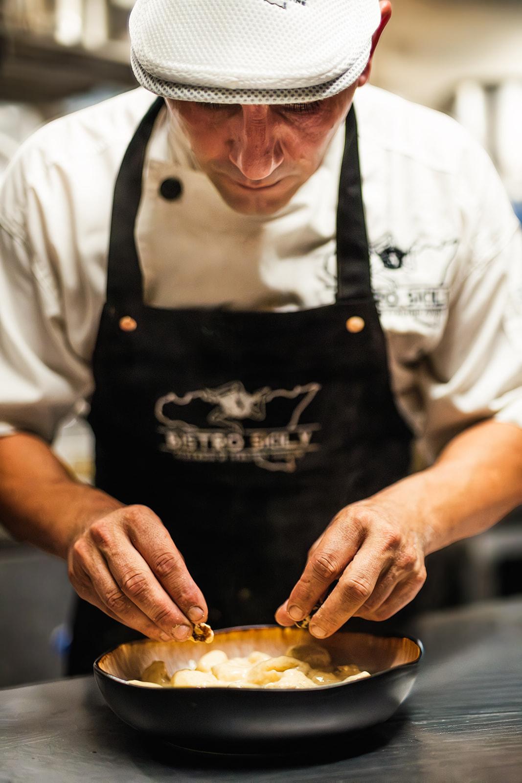 A chef in a branded Bistro Sicily apron plating gnocchi by hand