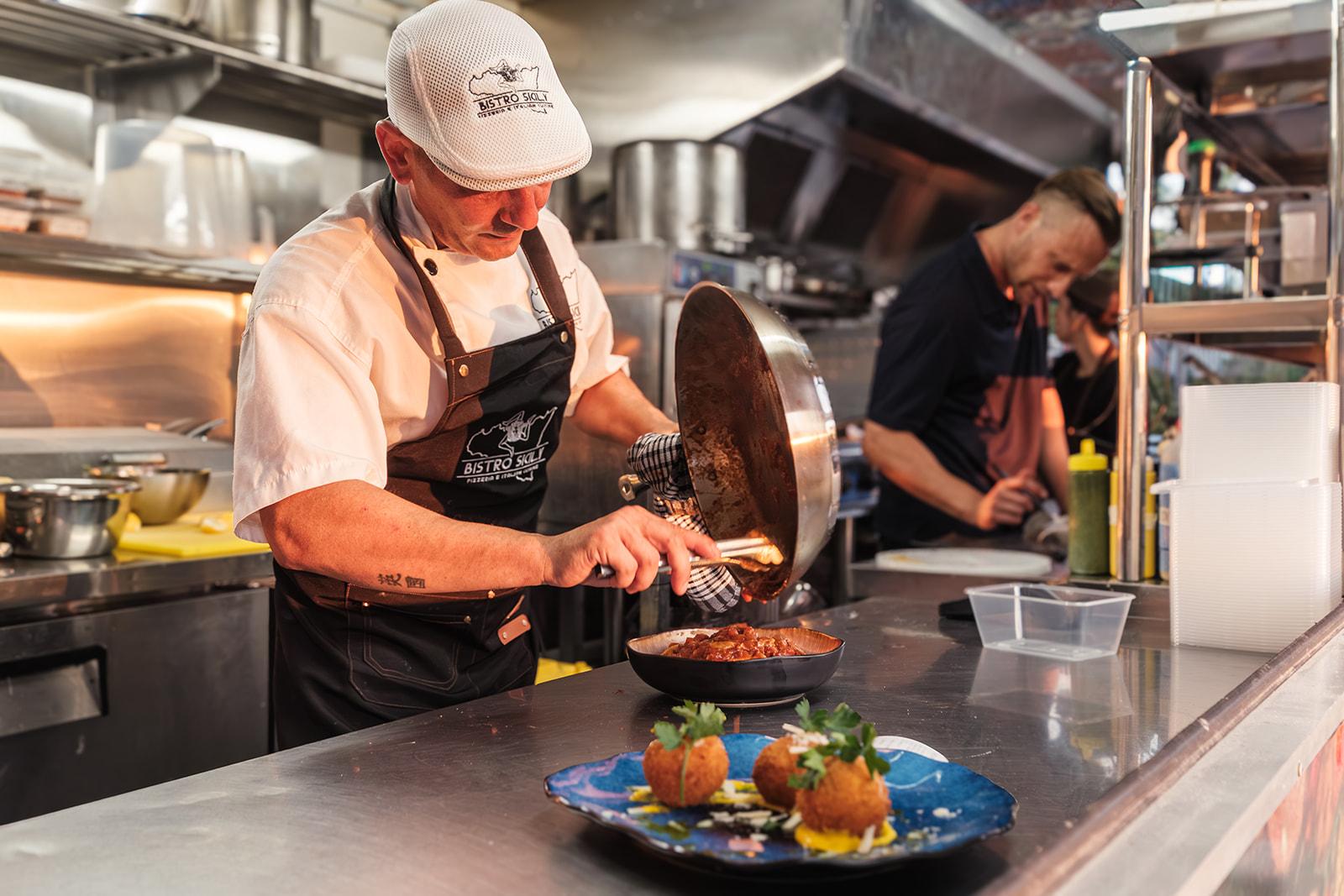 Giuseppe plating arancini in the kitchen, staff working behind him