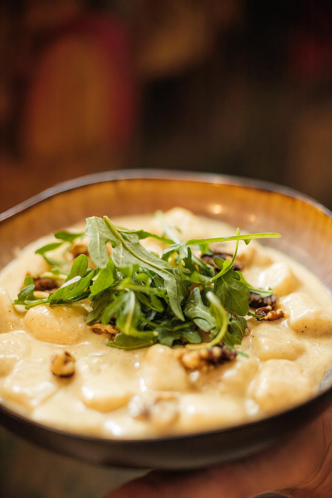 A bowl of gnocchi in a creamy sauce, topped with walnuts and rocket