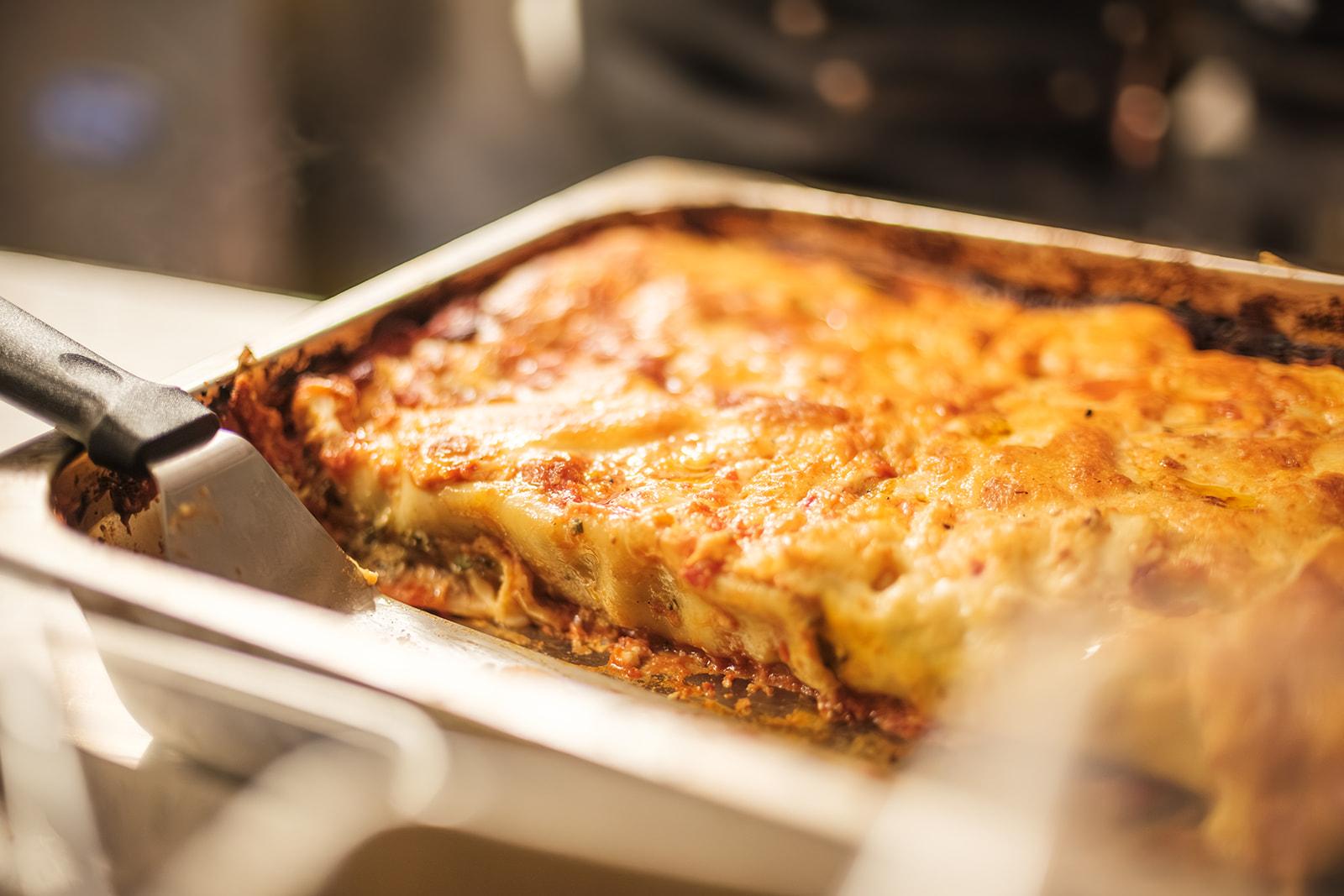 A tray of baked lasagna, a slice being lifted out with a spatula