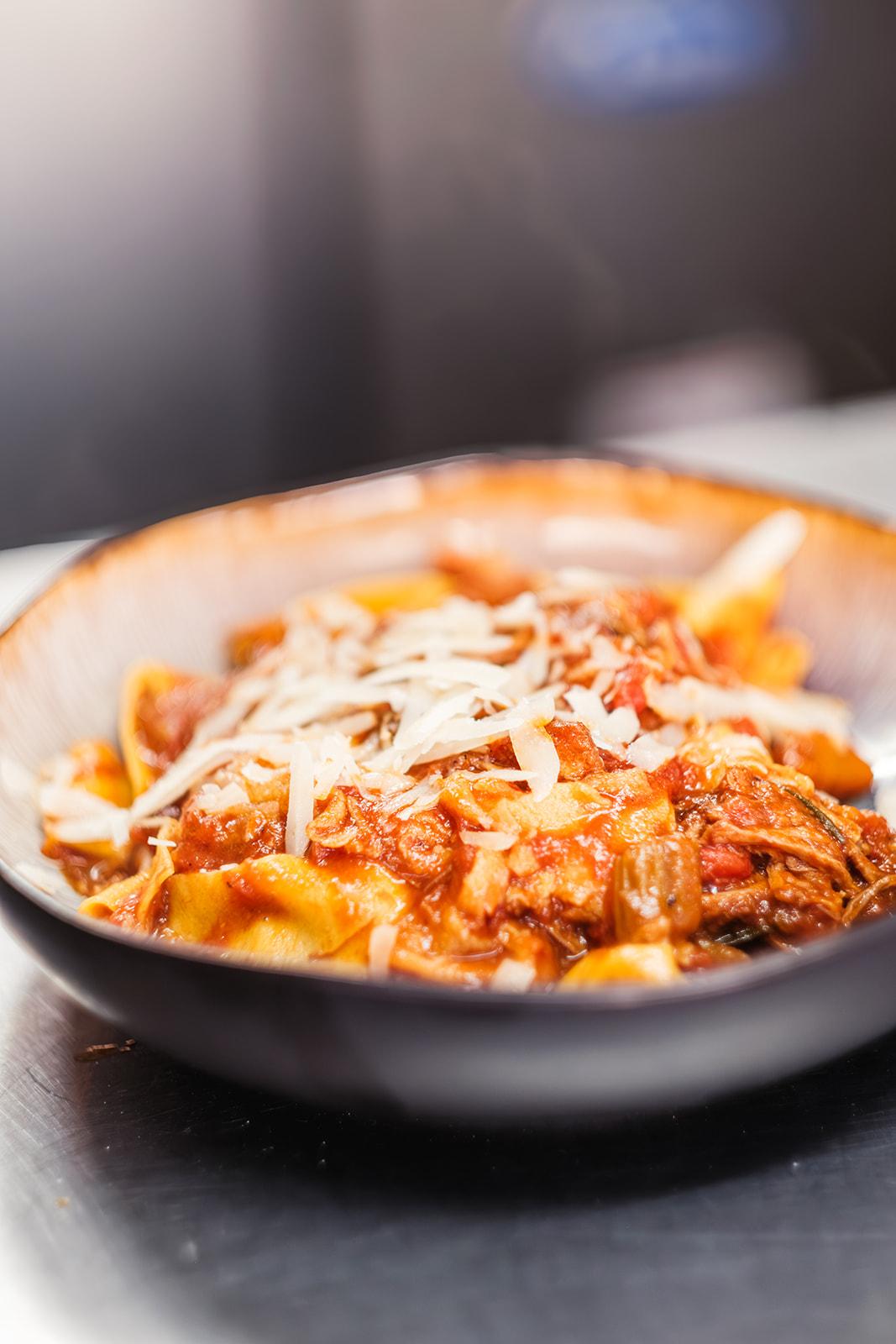 A bowl of pappardelle in a slow-cooked ragu, topped with shaved parmesan