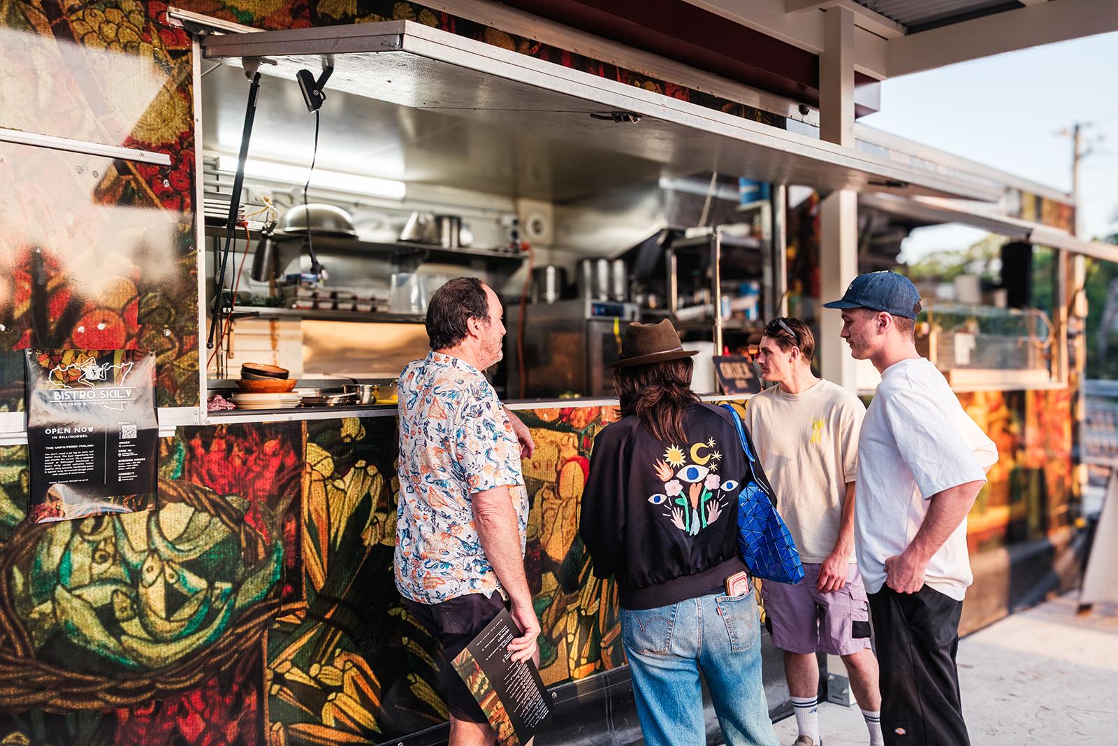 Customers queuing at the mural-painted Bistro Sicily food truck in the evening light