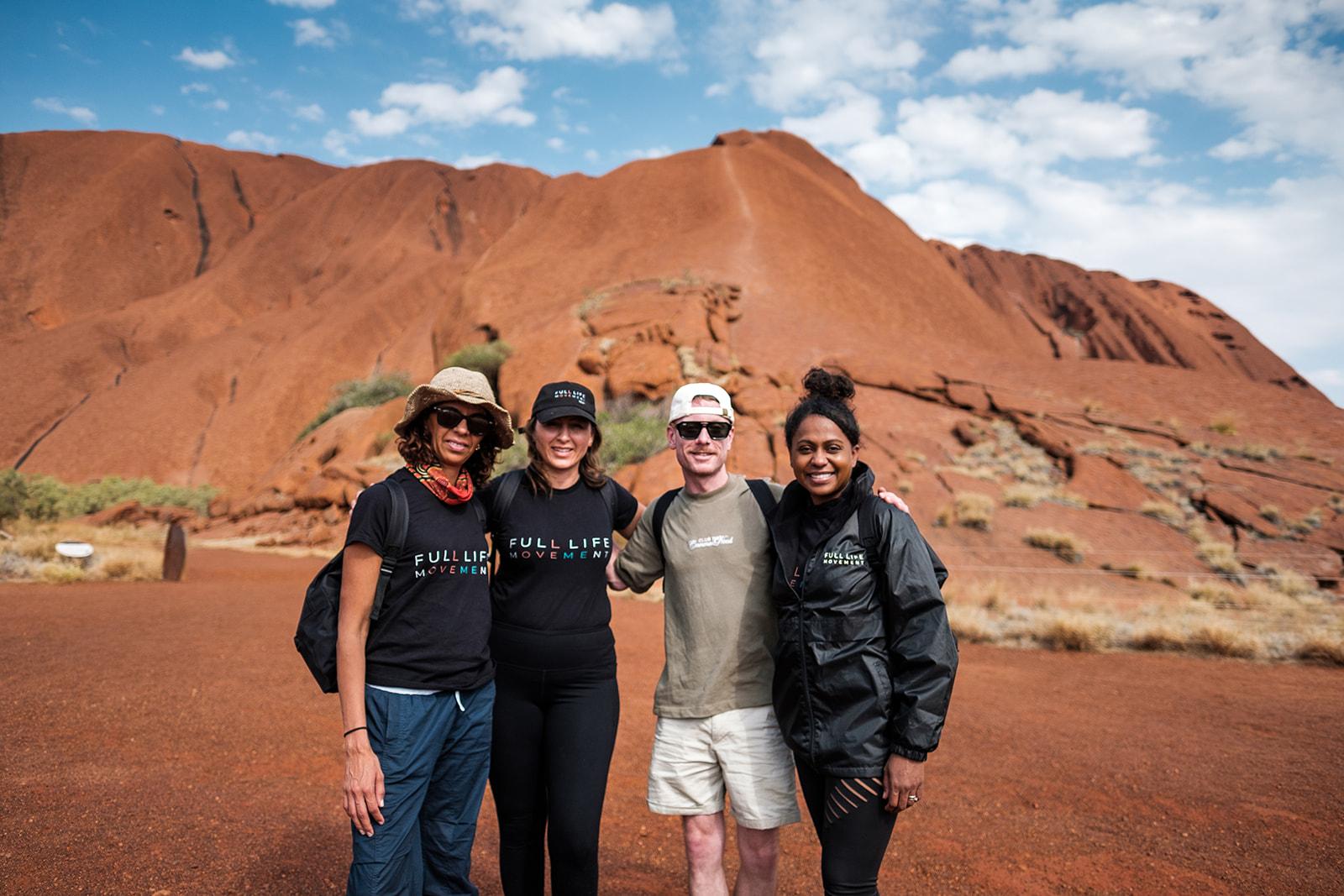 Four participants in branded Full Life Movement shirts standing together in front of Uluru