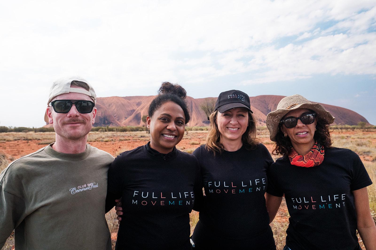 A small group in branded shirts posing in front of Uluru