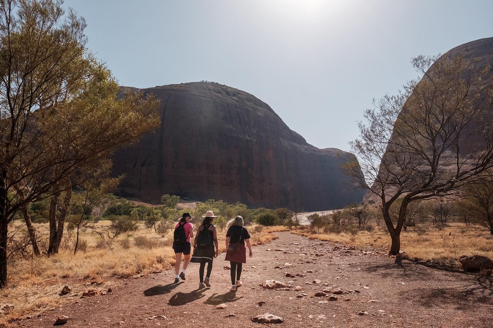 Two people walking a red dirt track toward Uluru in the distance