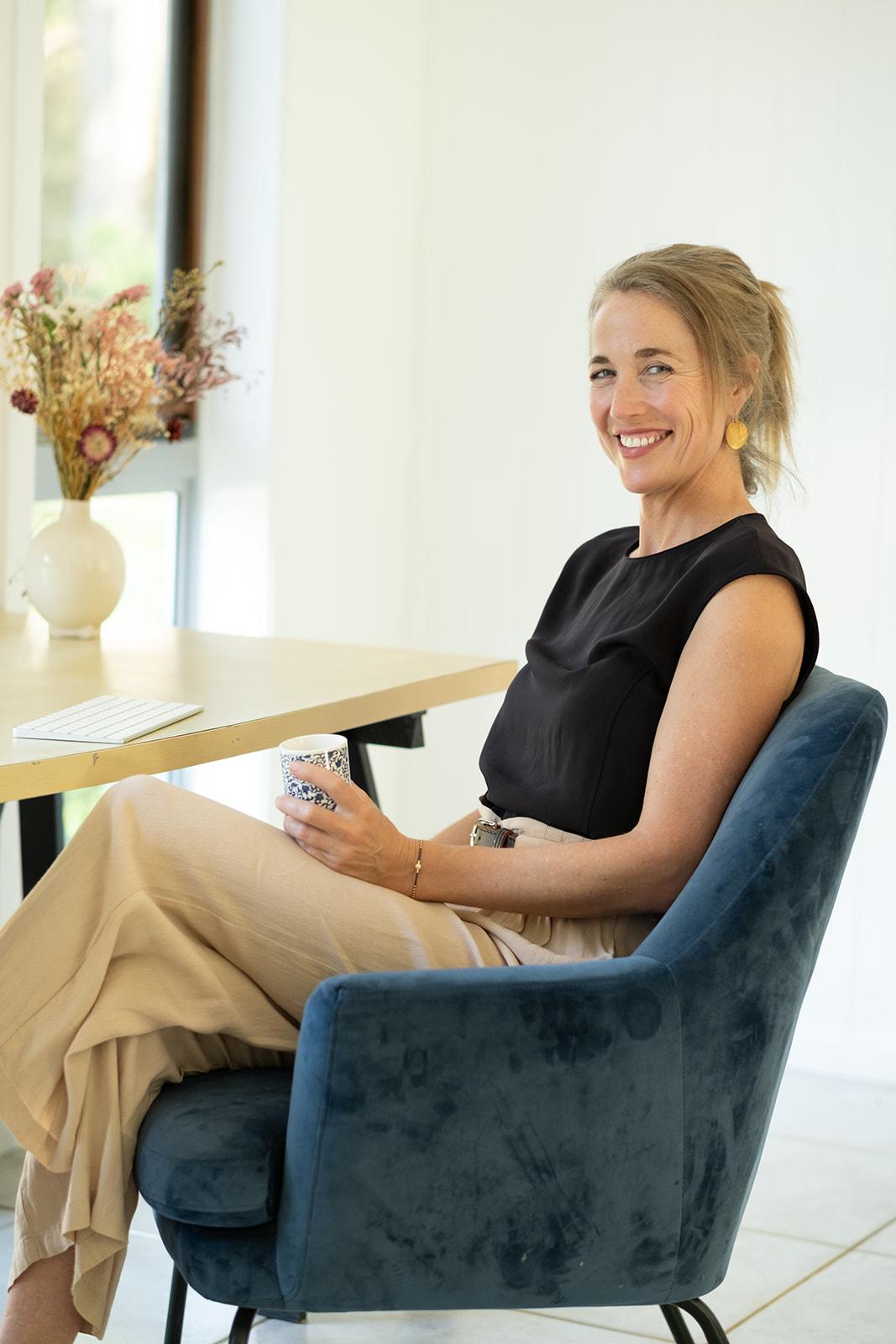 Grace Hawkins seated at a desk holding a teacup, a vase of dried flowers beside her