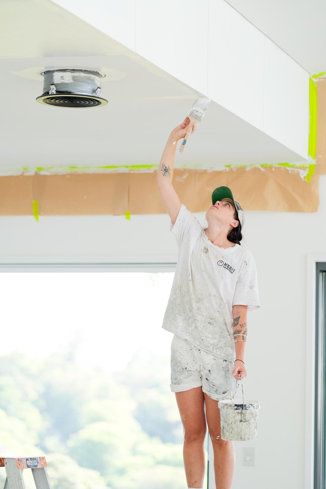 A painter reaching up to cut in a ceiling soffit, paint bucket in hand