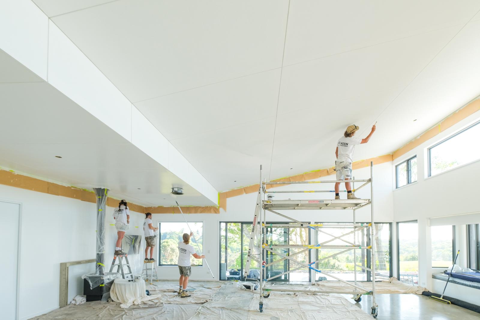 Three crew members from behind in a bright vaulted room, Keen Painters printed across the back of a shirt