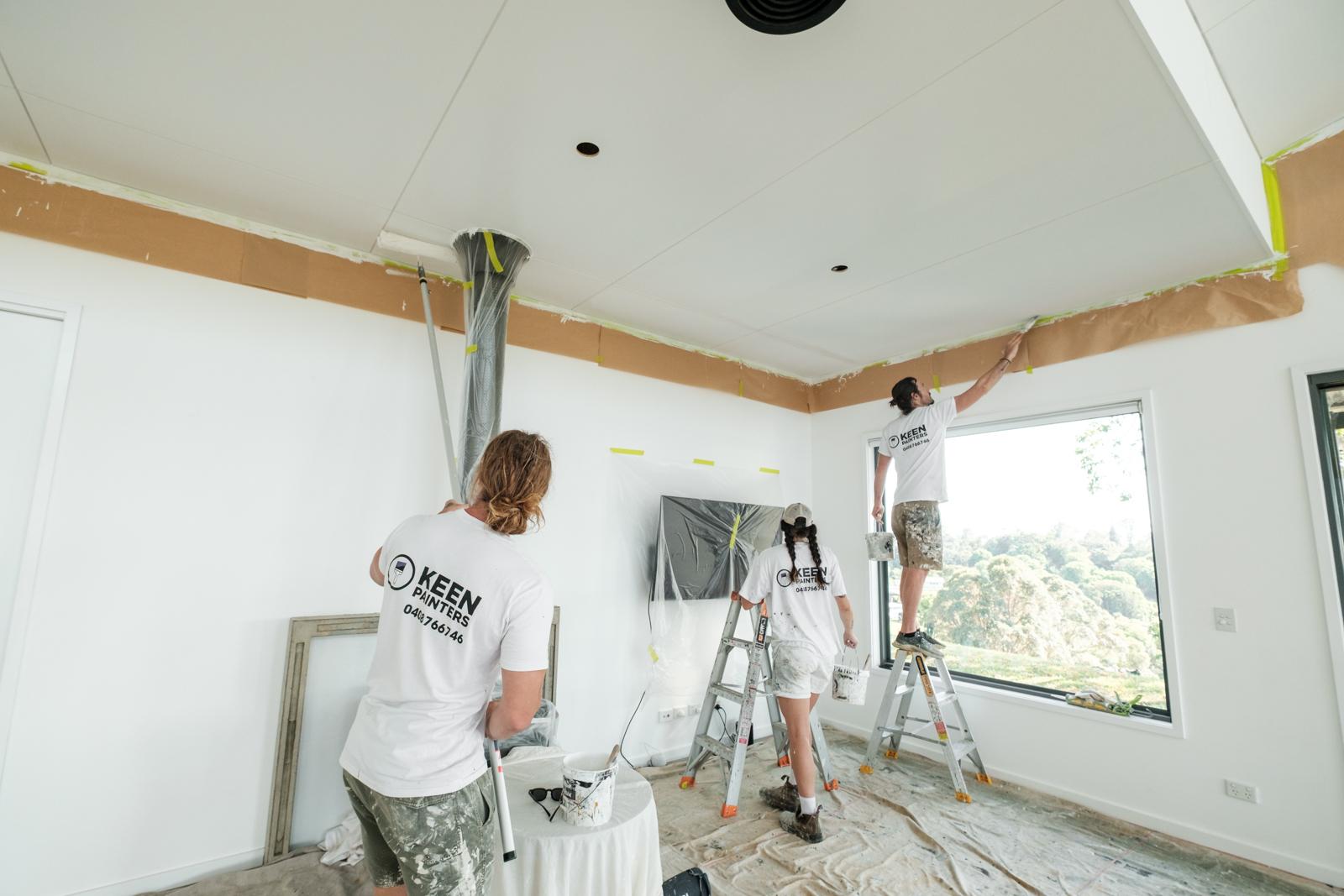The crew painting a large vaulted living room, one on a scaffold tower reaching the ceiling apex