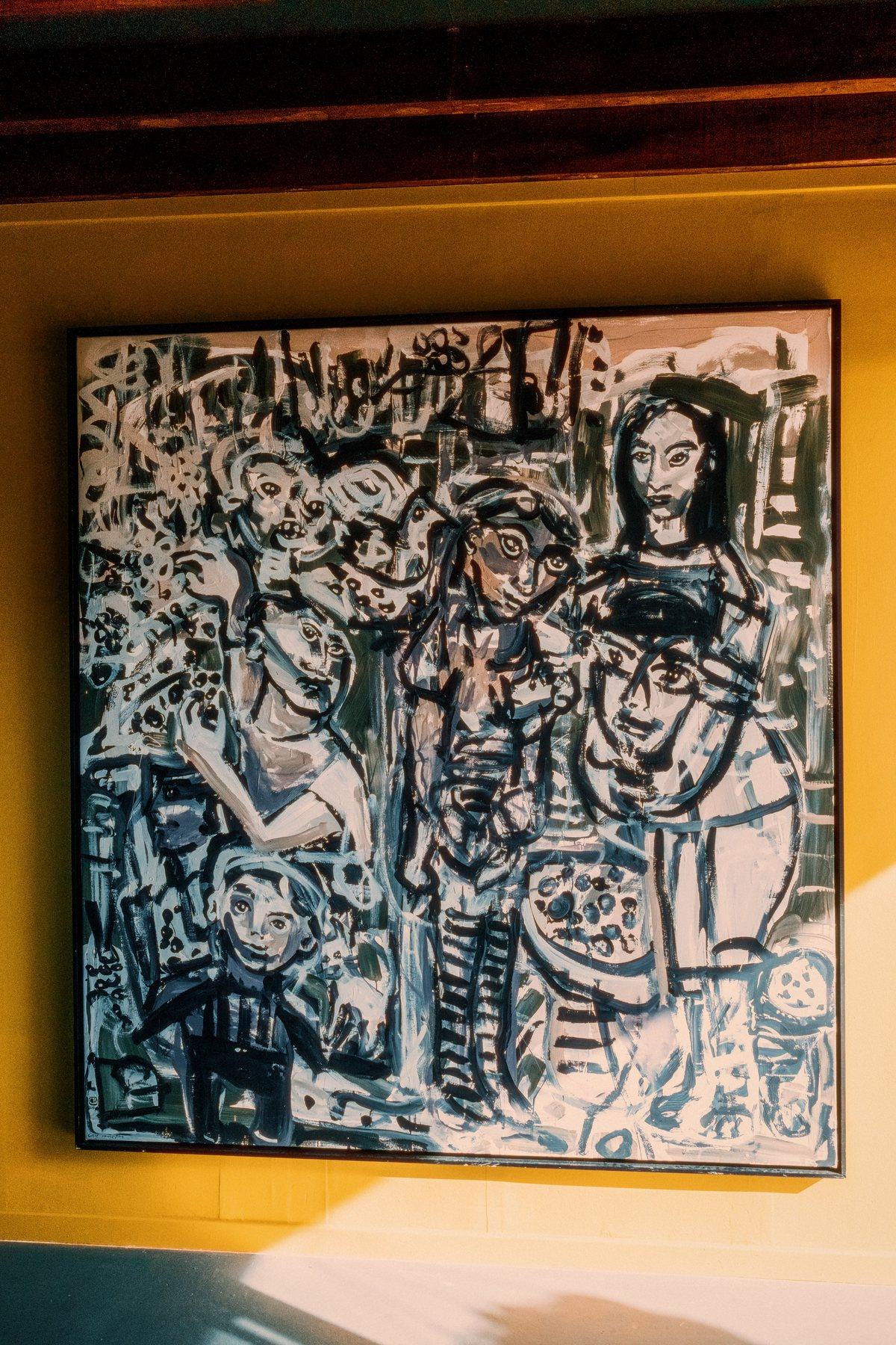A framed black and white painting hanging on a mustard-yellow wall