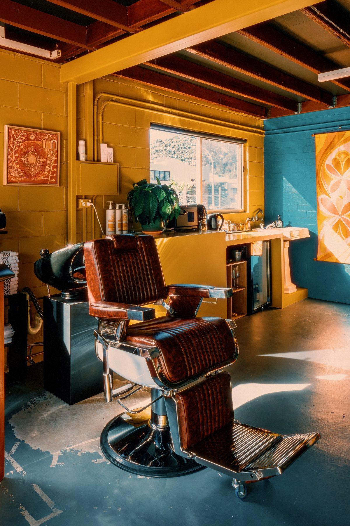 Barber chair beside the wash basin, framed Aboriginal artwork on the mustard wall