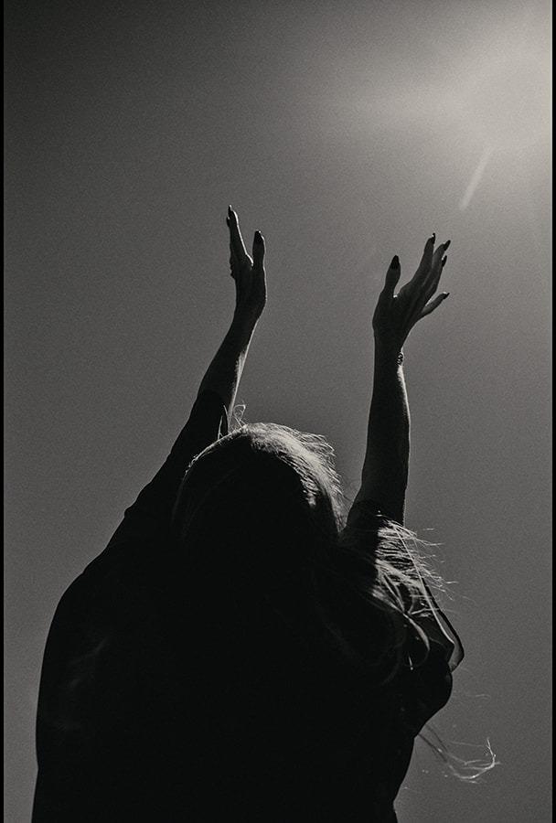A woman raising both arms overhead against a bright sky, black and white