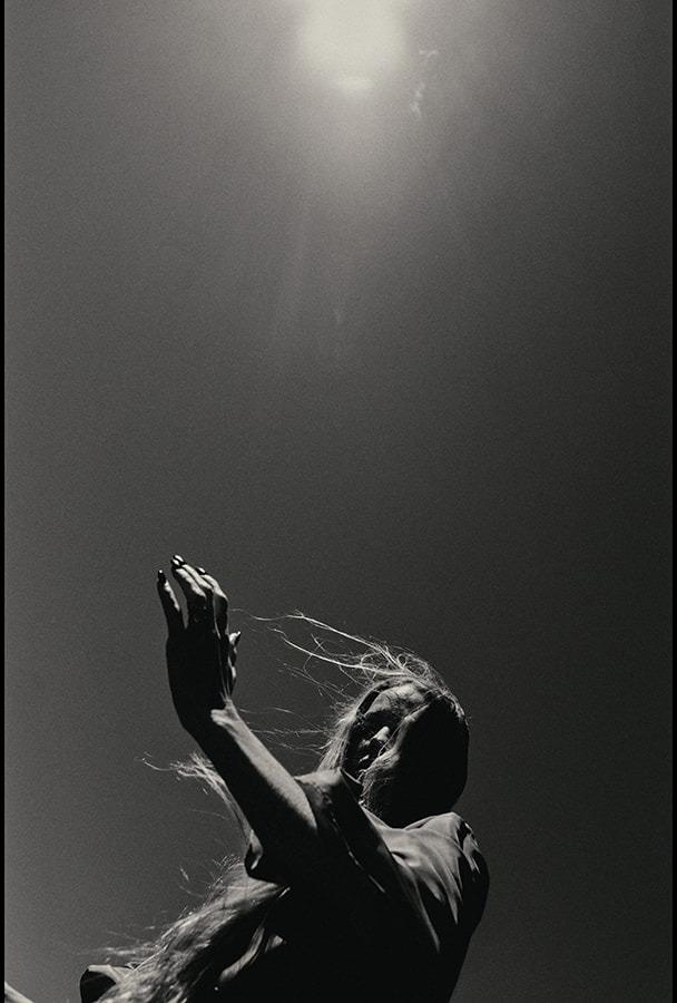A woman with one arm raised against a sun flare, black and white