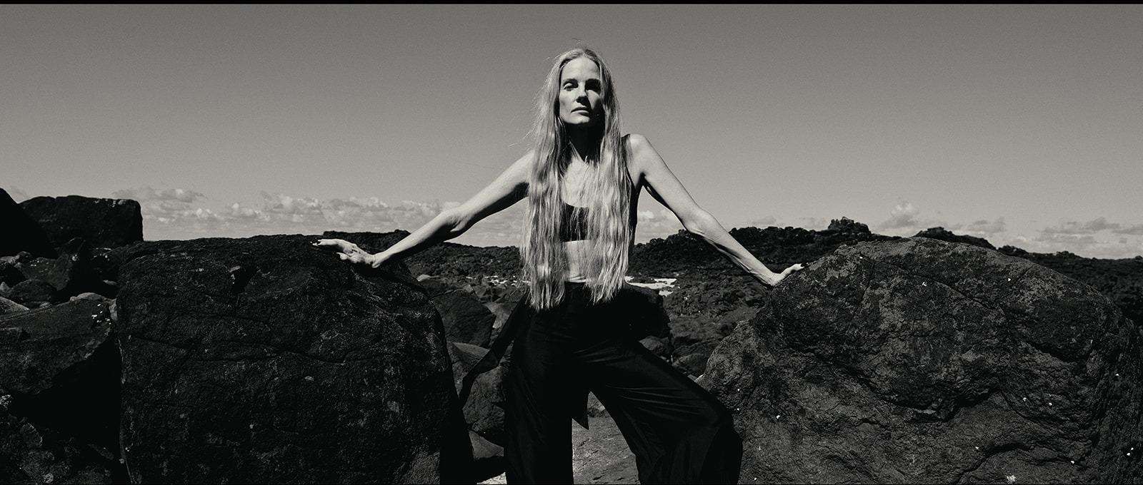 A woman standing on the rocks with arms outstretched, black and white
