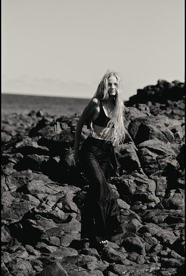 A woman in black on the rocks, hair blowing in the wind, black and white