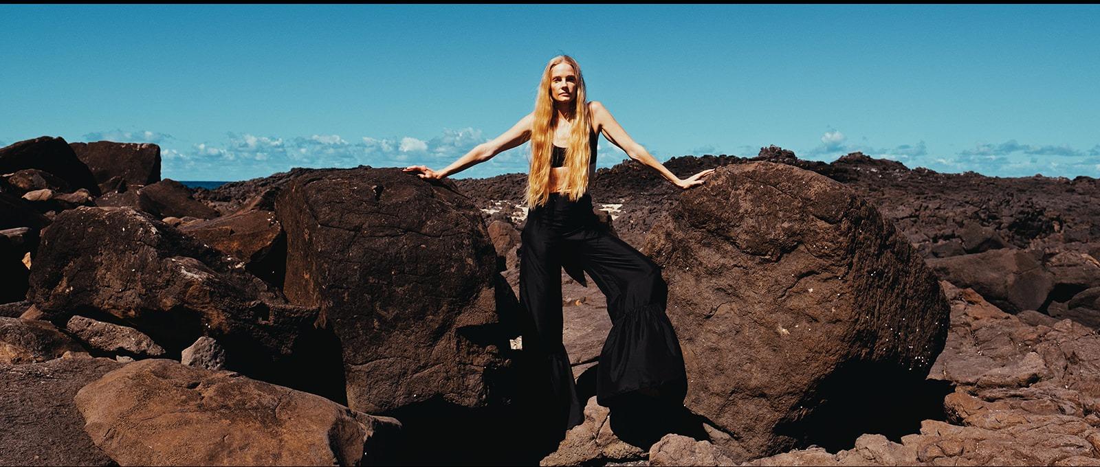 A woman in black standing on the rocks against a clear blue sky