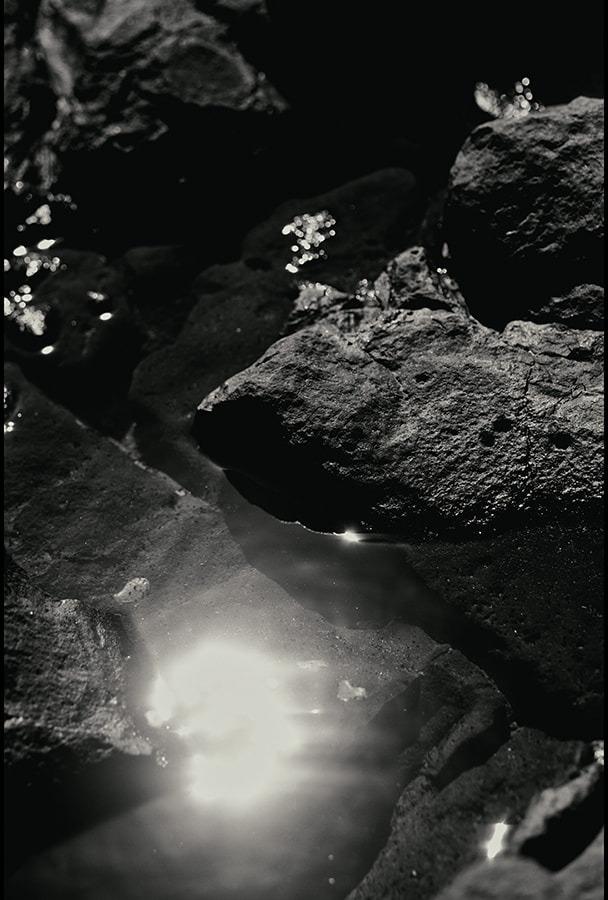 Close detail of a tide pool between dark rocks, light reflecting on the water, black and white