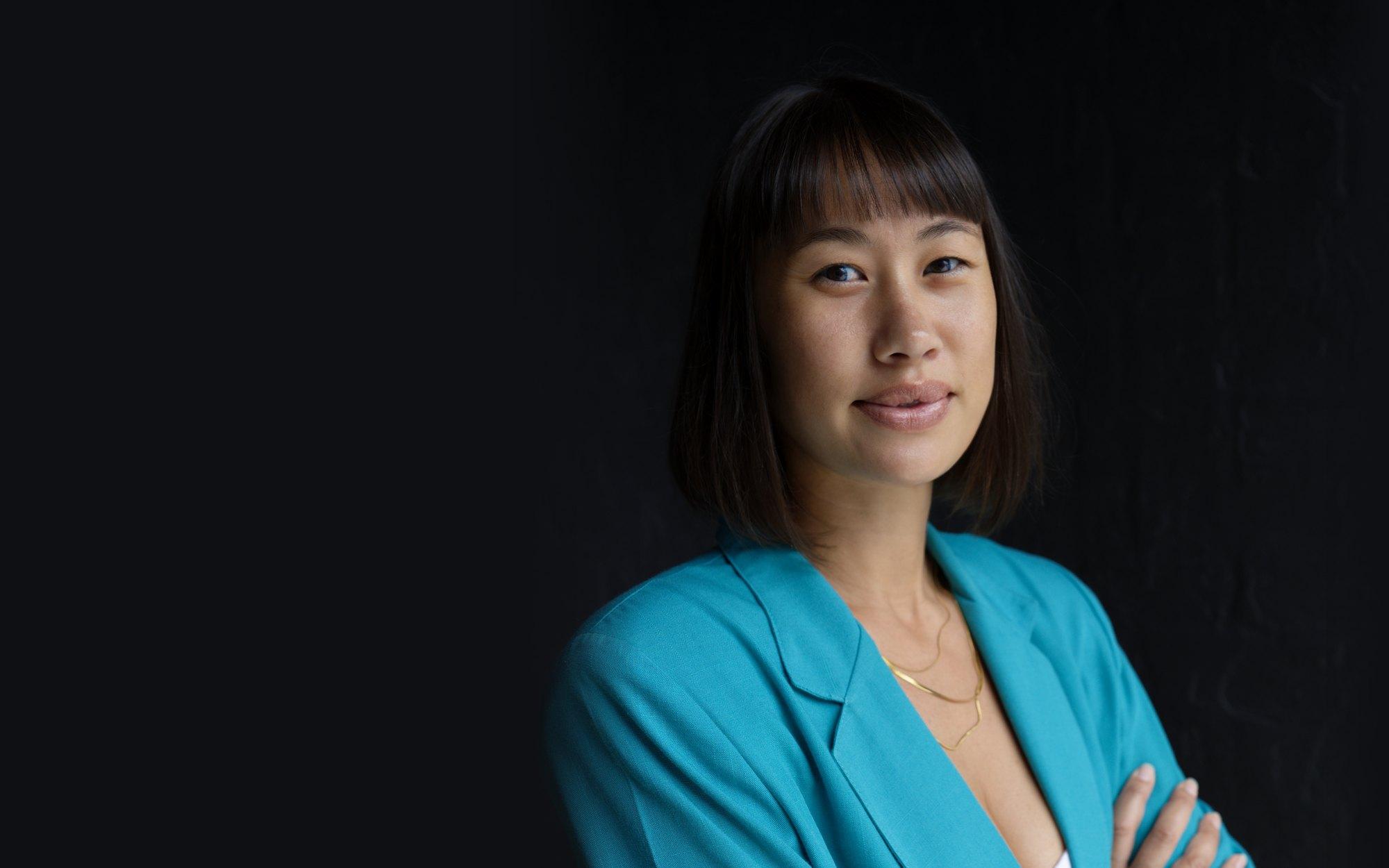 Roxy, founder of The Wedding Agency, in a bright teal blazer against a dark backdrop