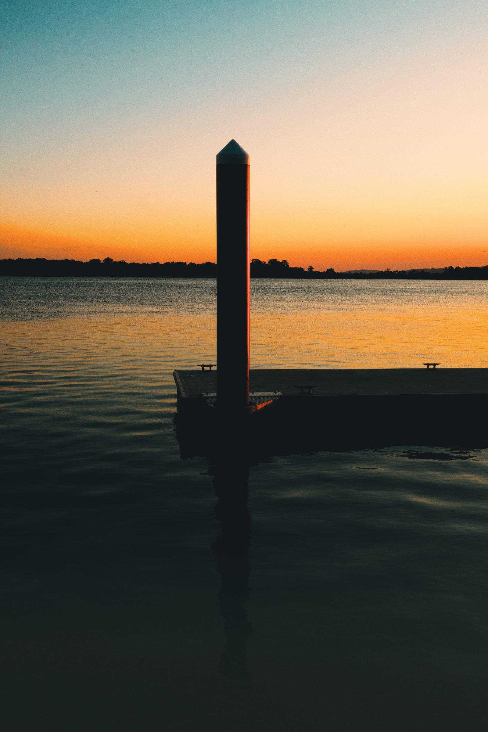 A jetty post silhouetted against an orange and teal sunset over the water