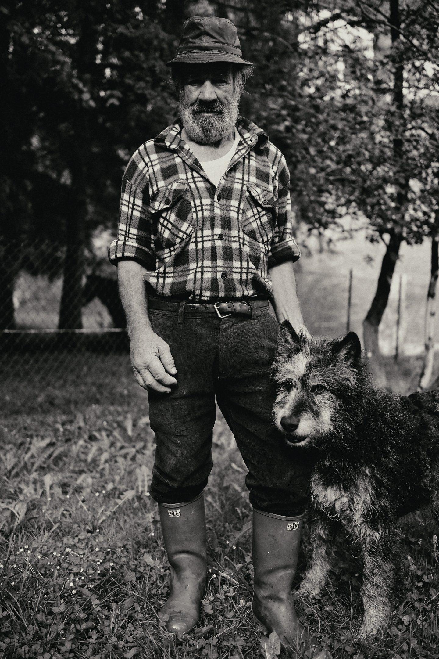 Black and white: a man in a checked shirt standing in a park with a dog