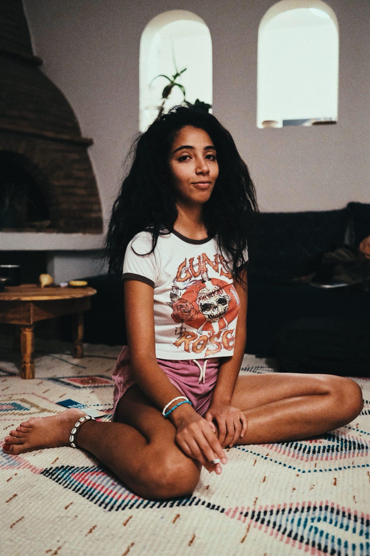 Yousra sitting cross-legged on a patterned rug in a whitewashed room with arched windows