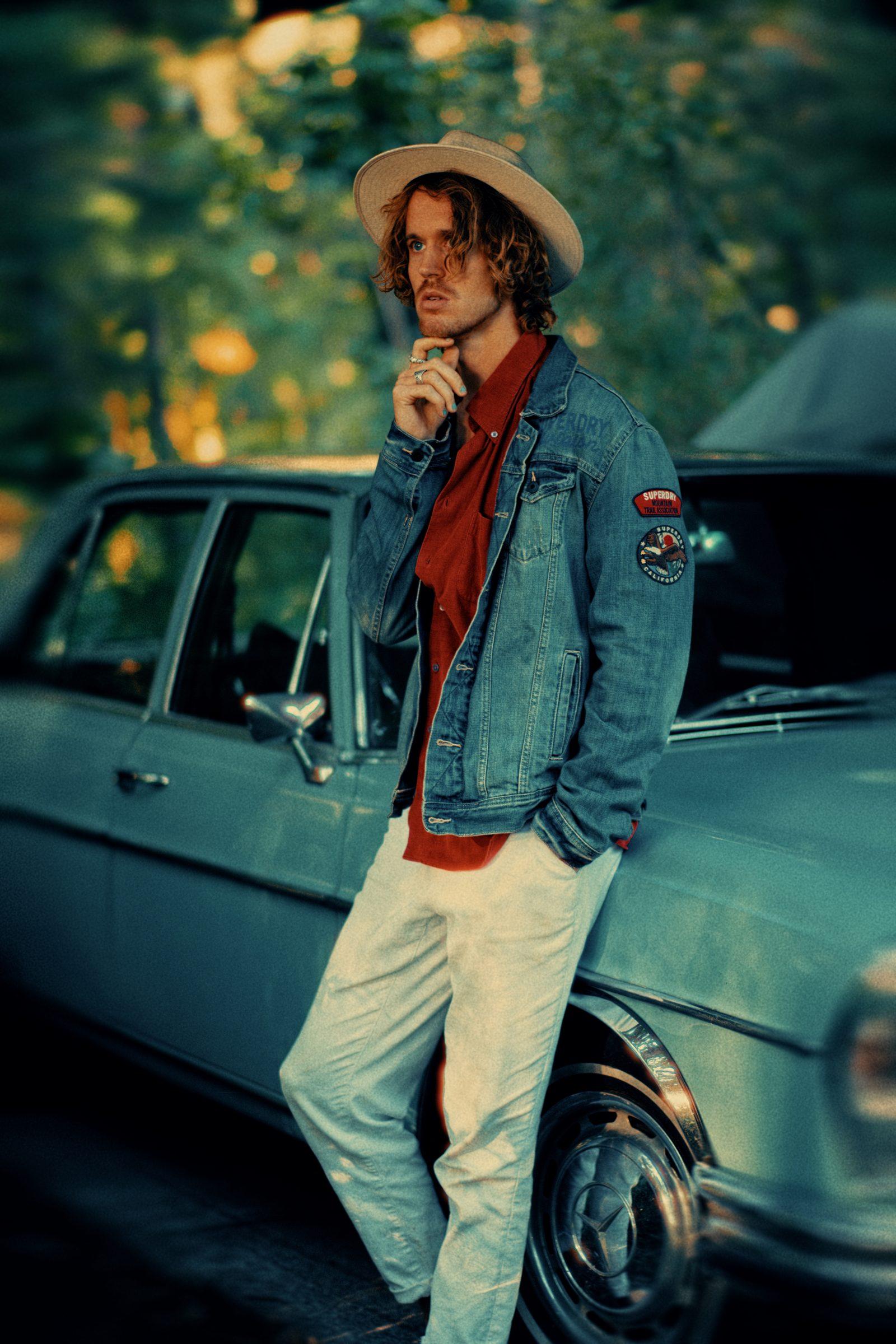 Kenzo Cruz in a denim jacket over a red shirt, leaning against a vintage car