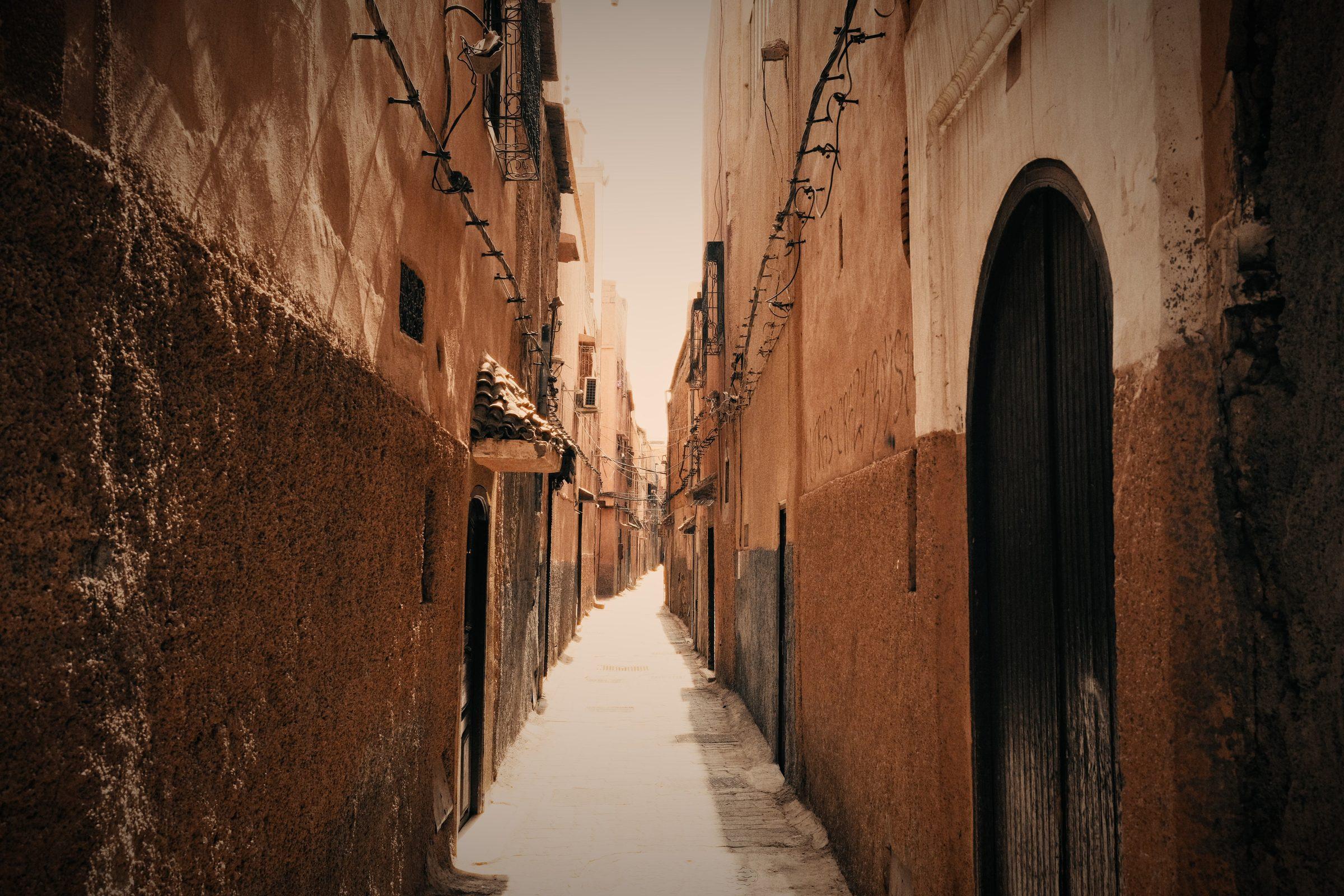 A long, narrow terracotta lane with a dark arched door and strings of lights overhead
