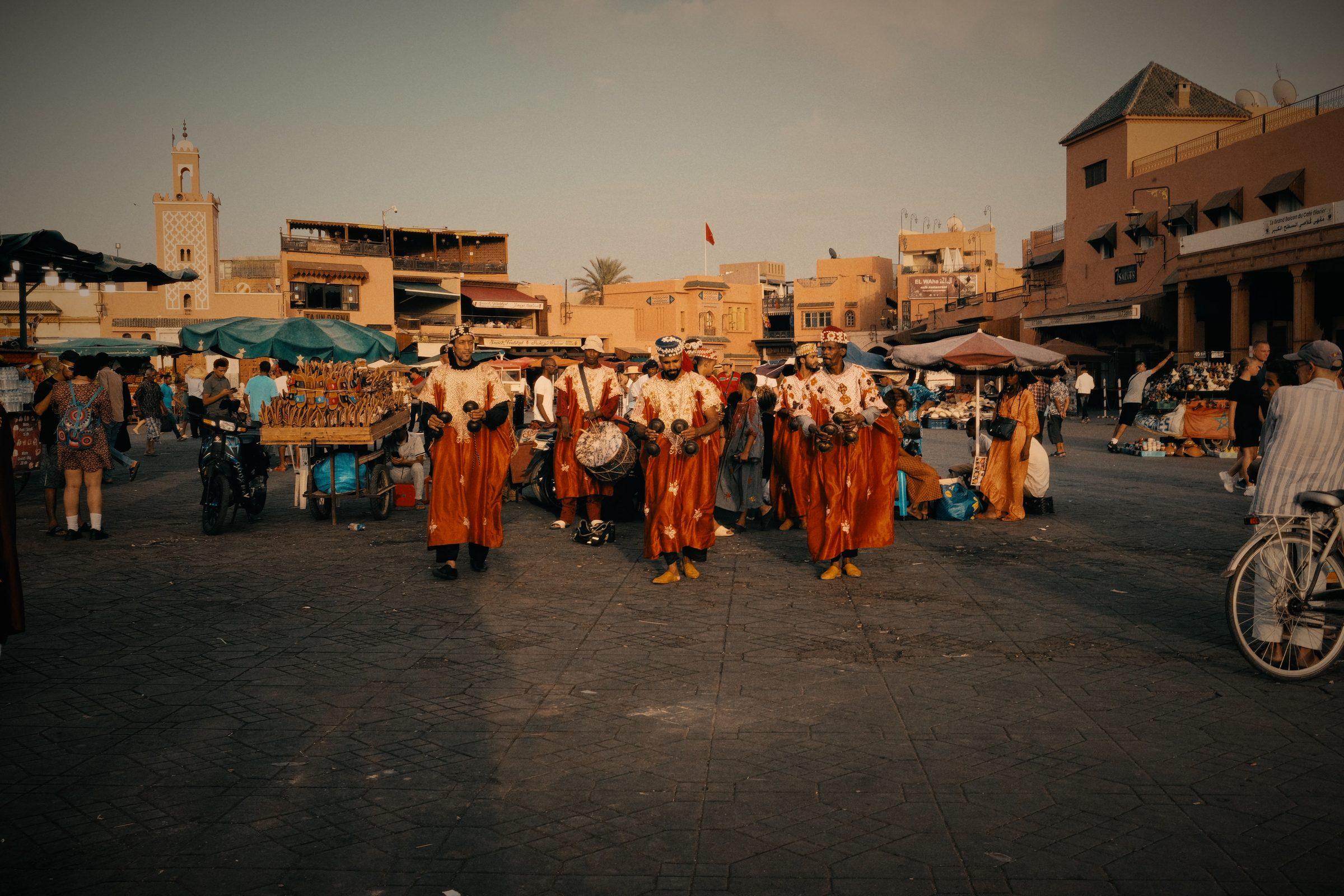 A line of drummers in orange robes crossing the square at dusk