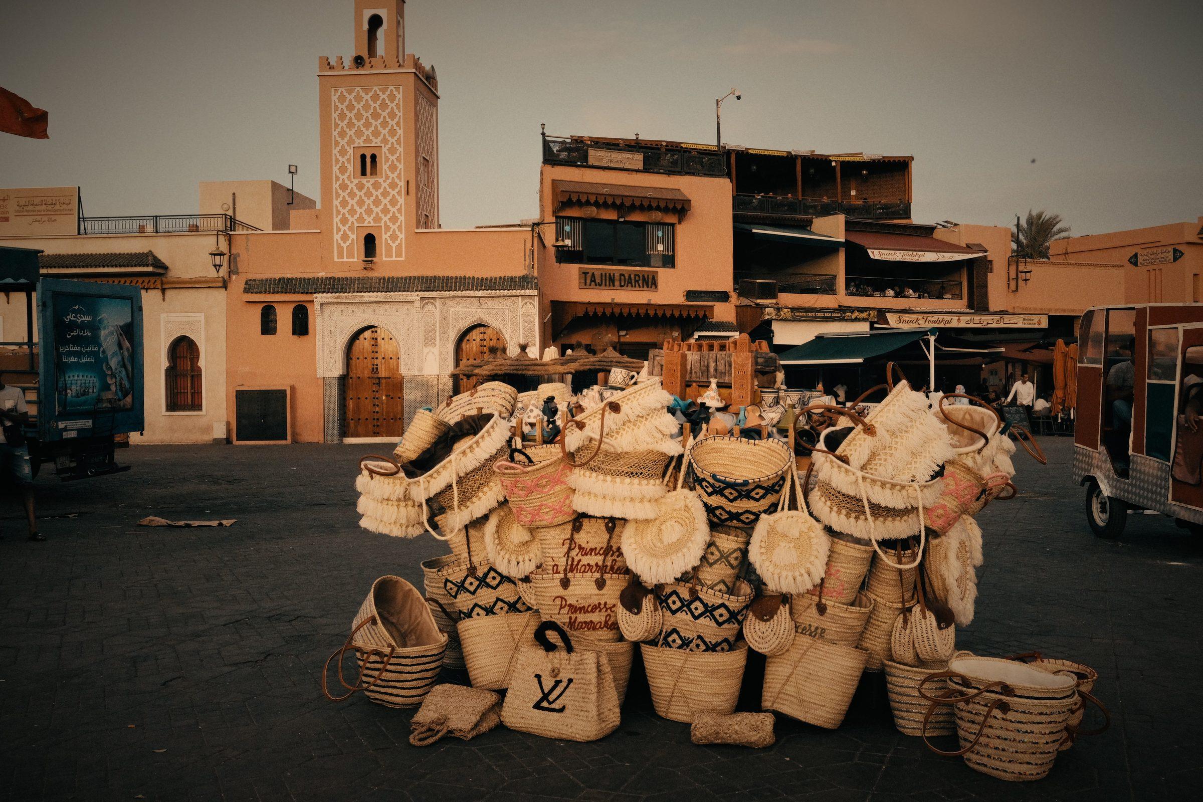 A heap of woven straw baskets in an empty square, a minaret and low buildings behind