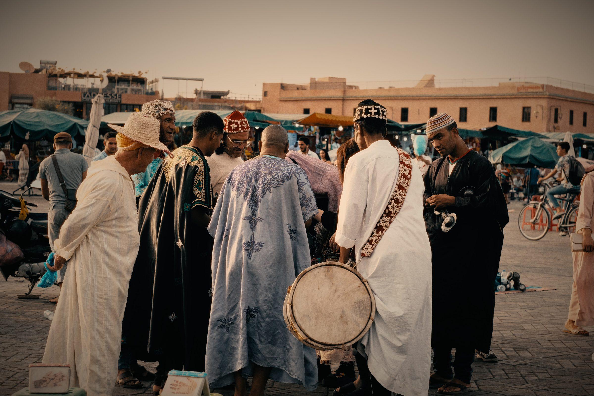 Men in robes of blue, green and white gathered in the square, one carrying a drum