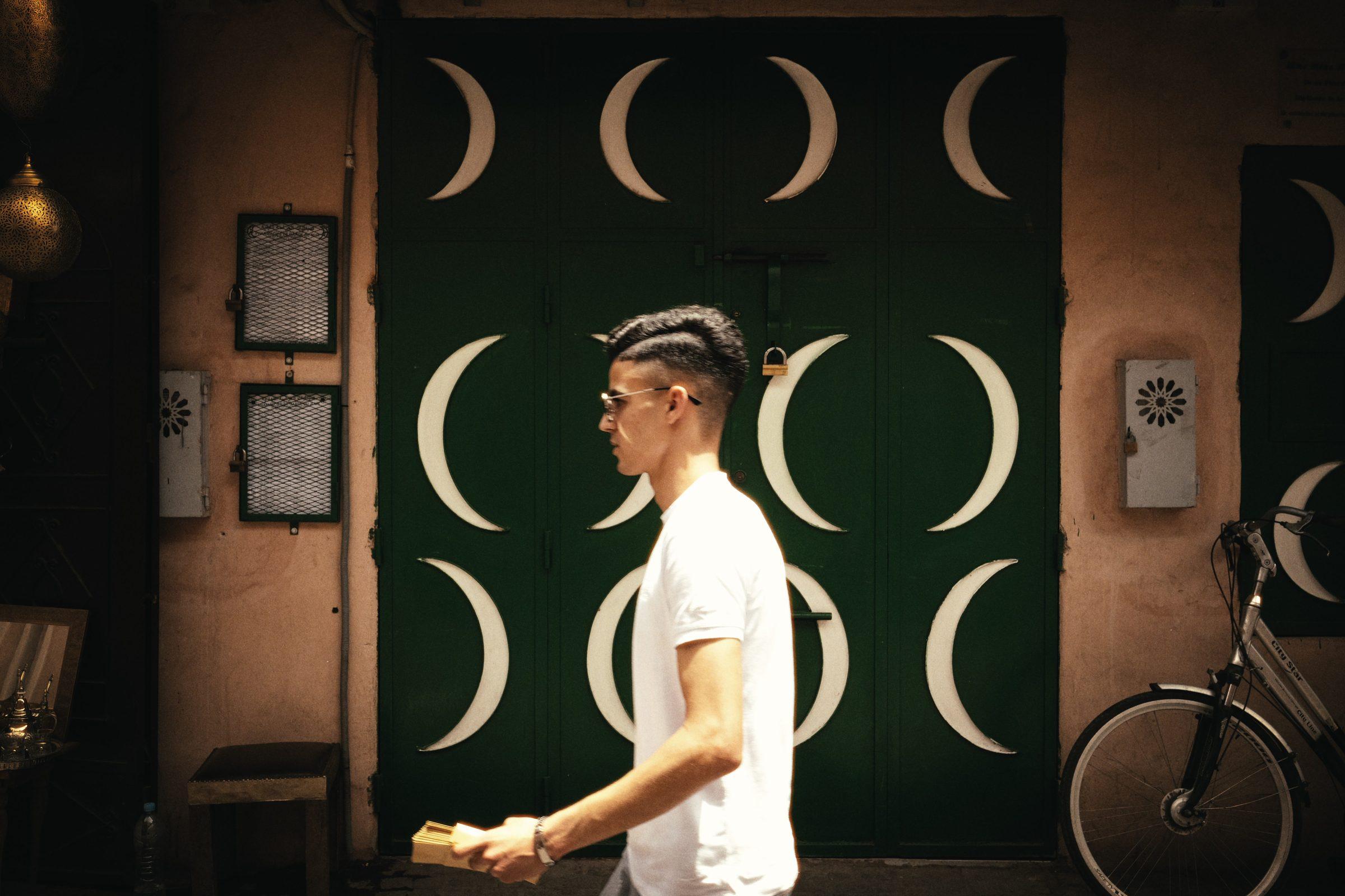 A man in a white T-shirt walks past a dark green door set with white crescent moons