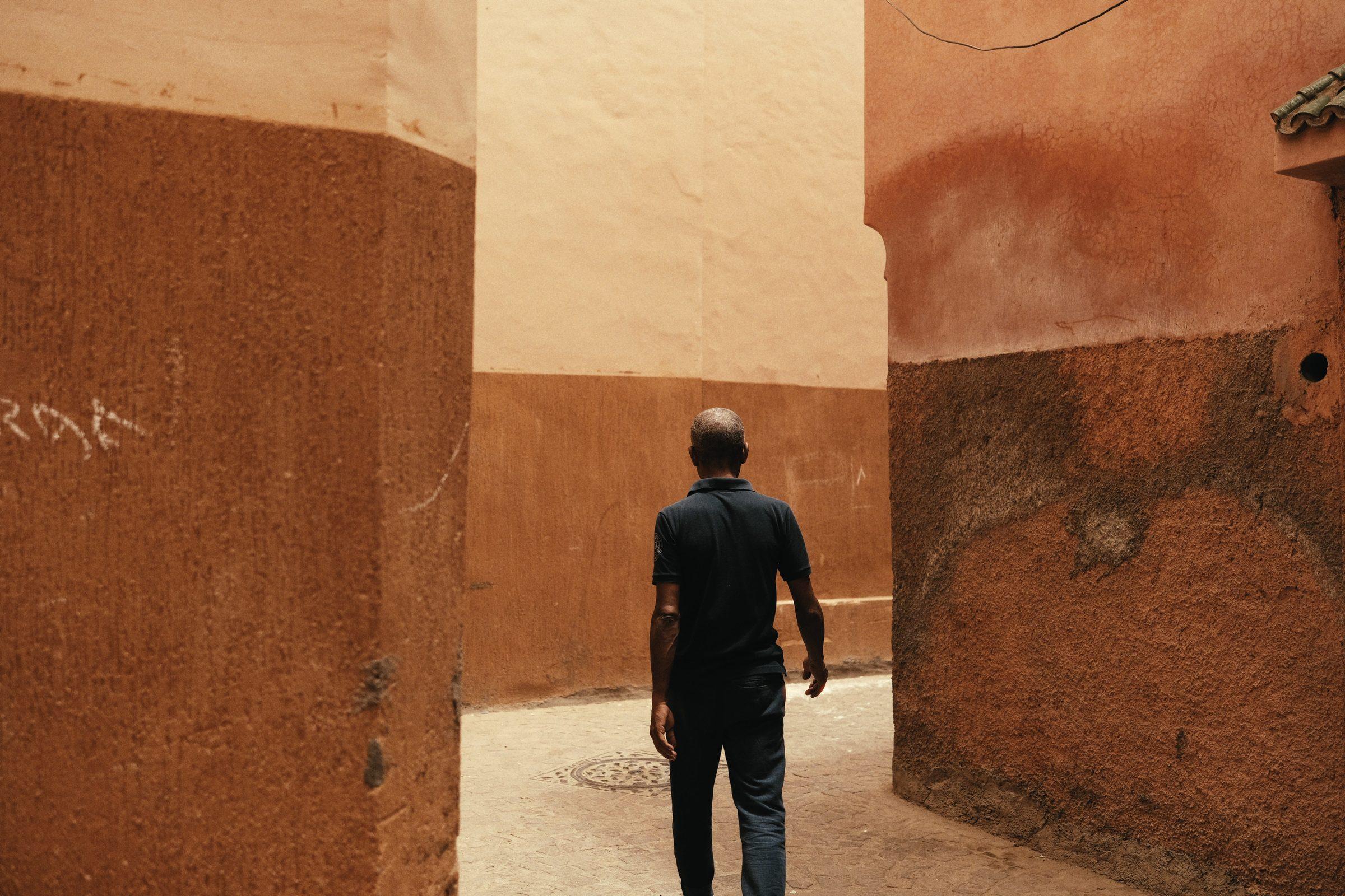 A man in dark clothes walks away down a narrow terracotta lane