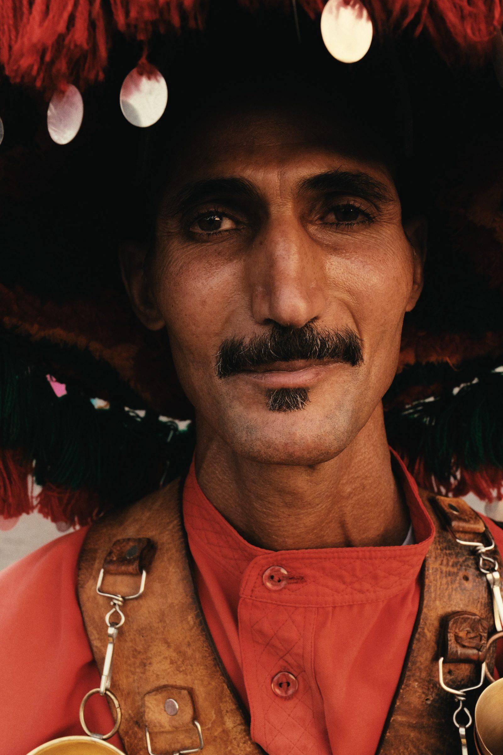 Close portrait of the water seller in his tasselled hat, brass cups across his chest