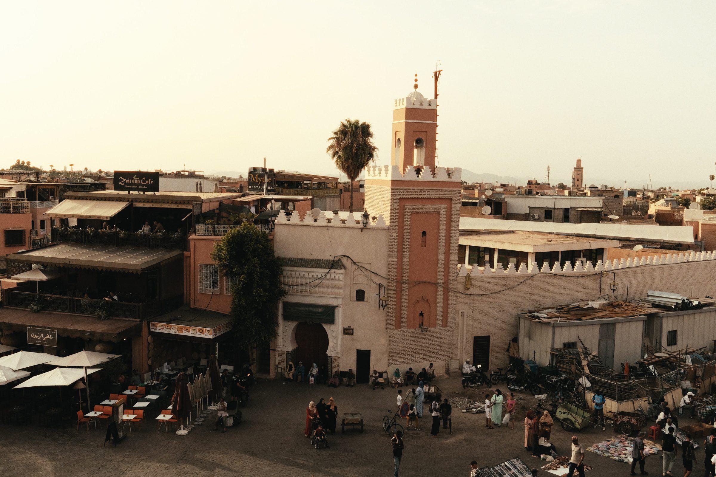 A rooftop view over the square and its minaret in warm evening light
