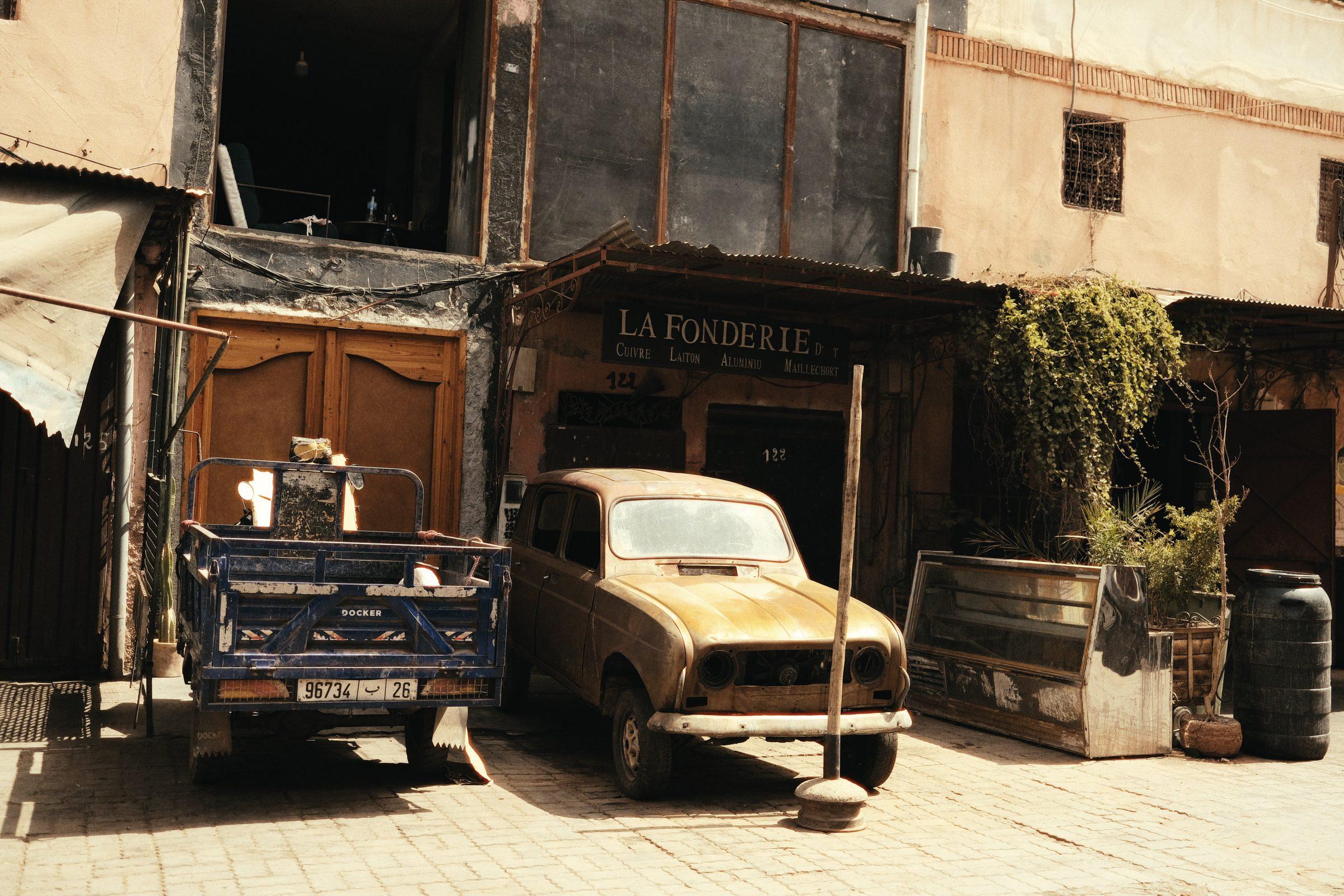 A vintage Renault 4 and a blue pickup parked outside an old workshop, "La Fonderie" painted above the door