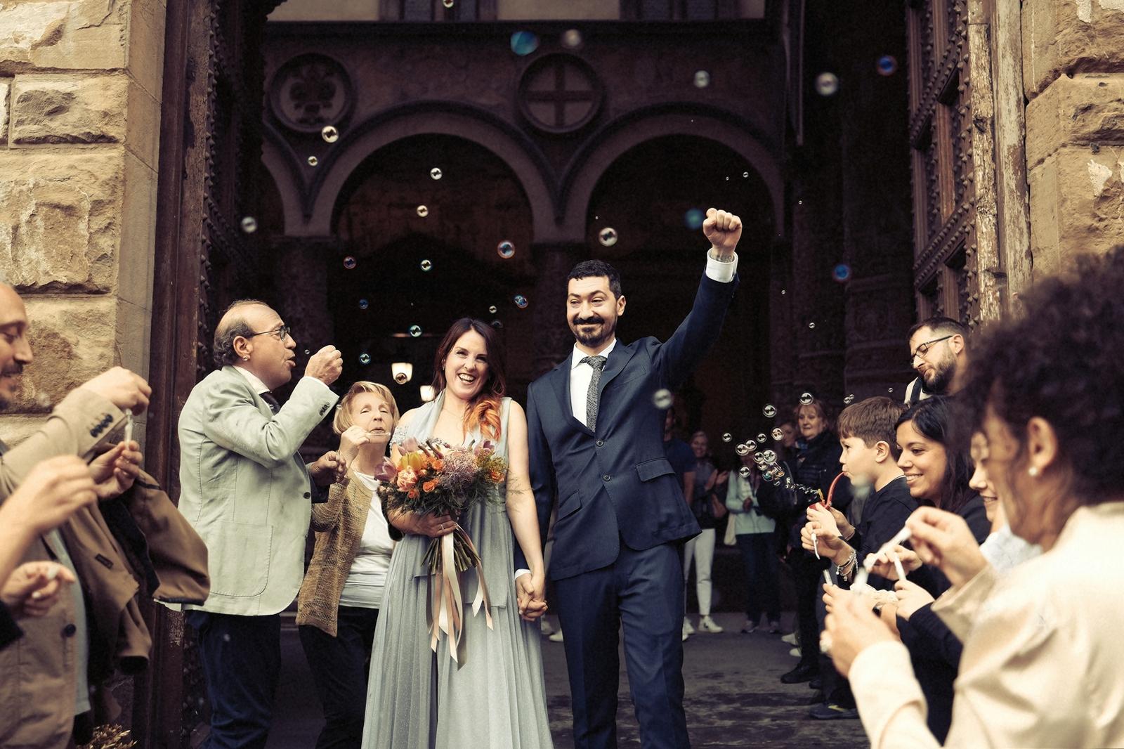 Newlyweds leaving the church through a crowd blowing bubbles, the groom's fist in the air