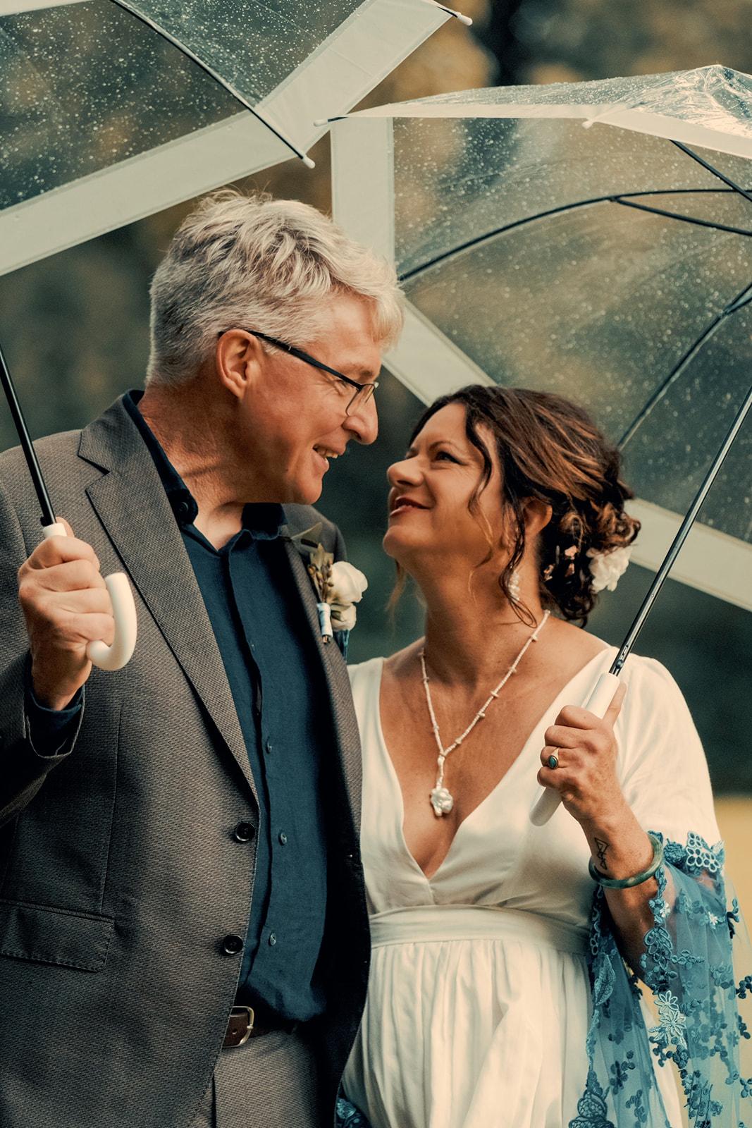 Kimberly and Andrew laughing together under two clear umbrellas in the rain