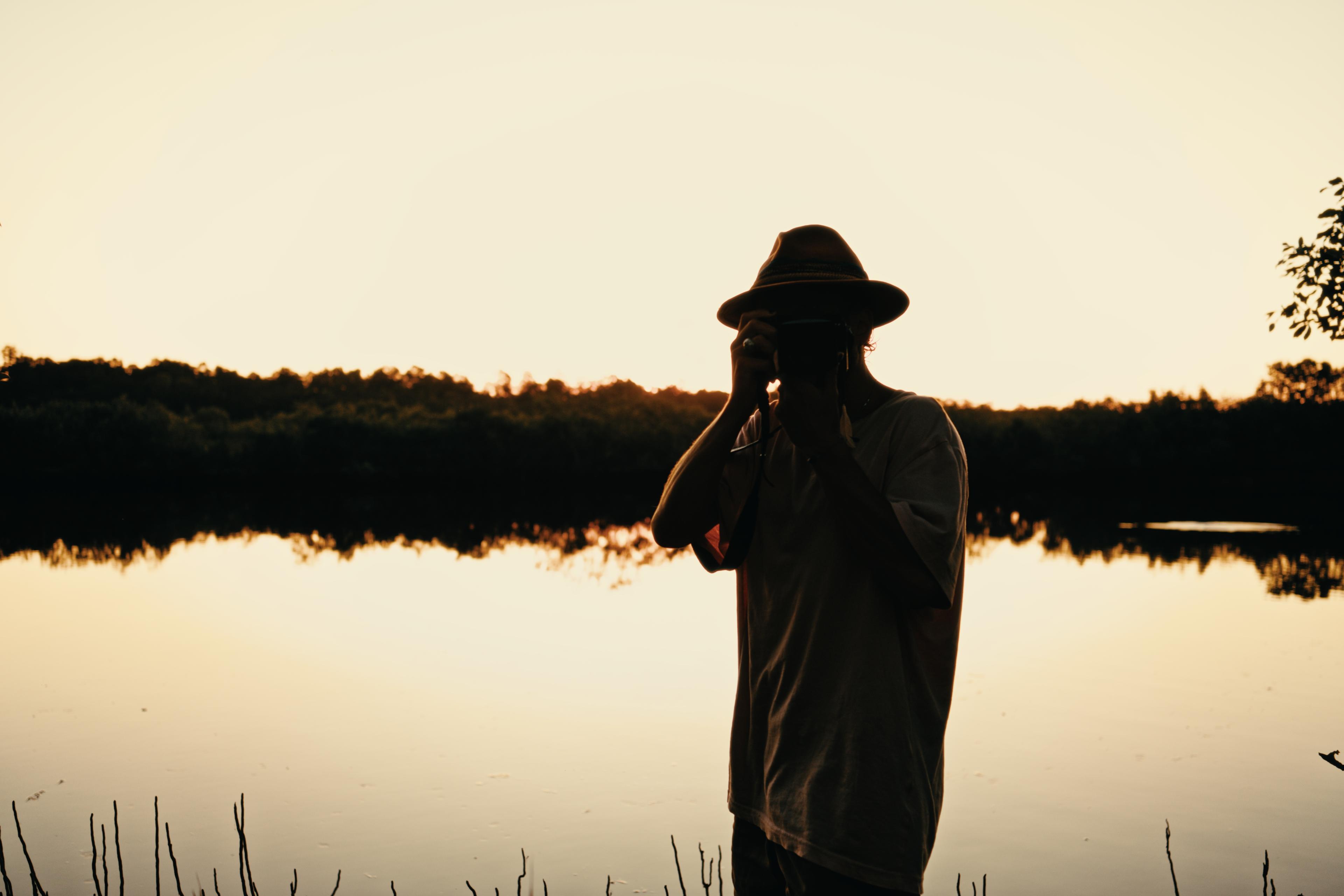 Silhouette of the same photographer by the lake at sunset, camera to his face