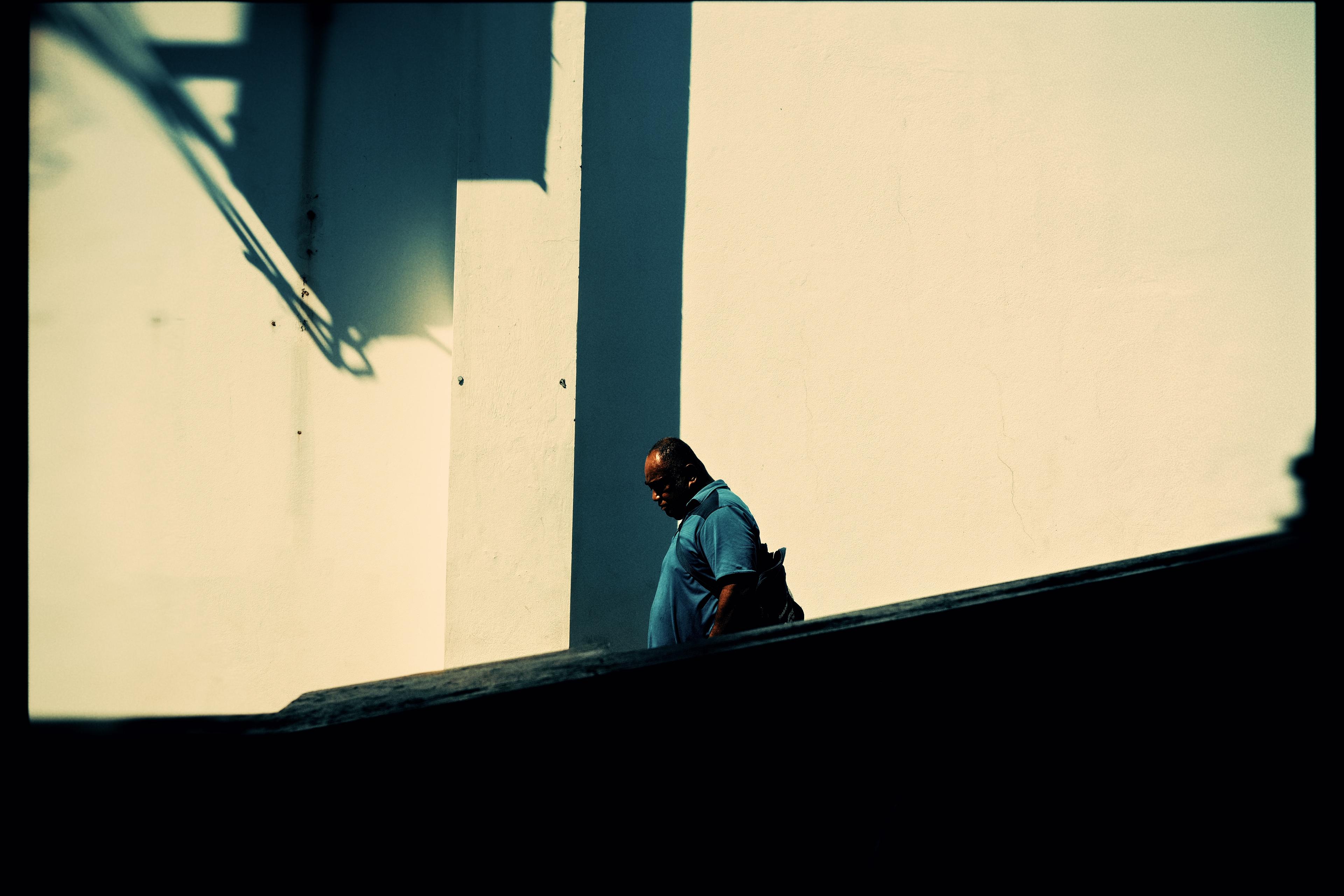 A man silhouetted against a sunlit wall, deep shadow cutting across the frame