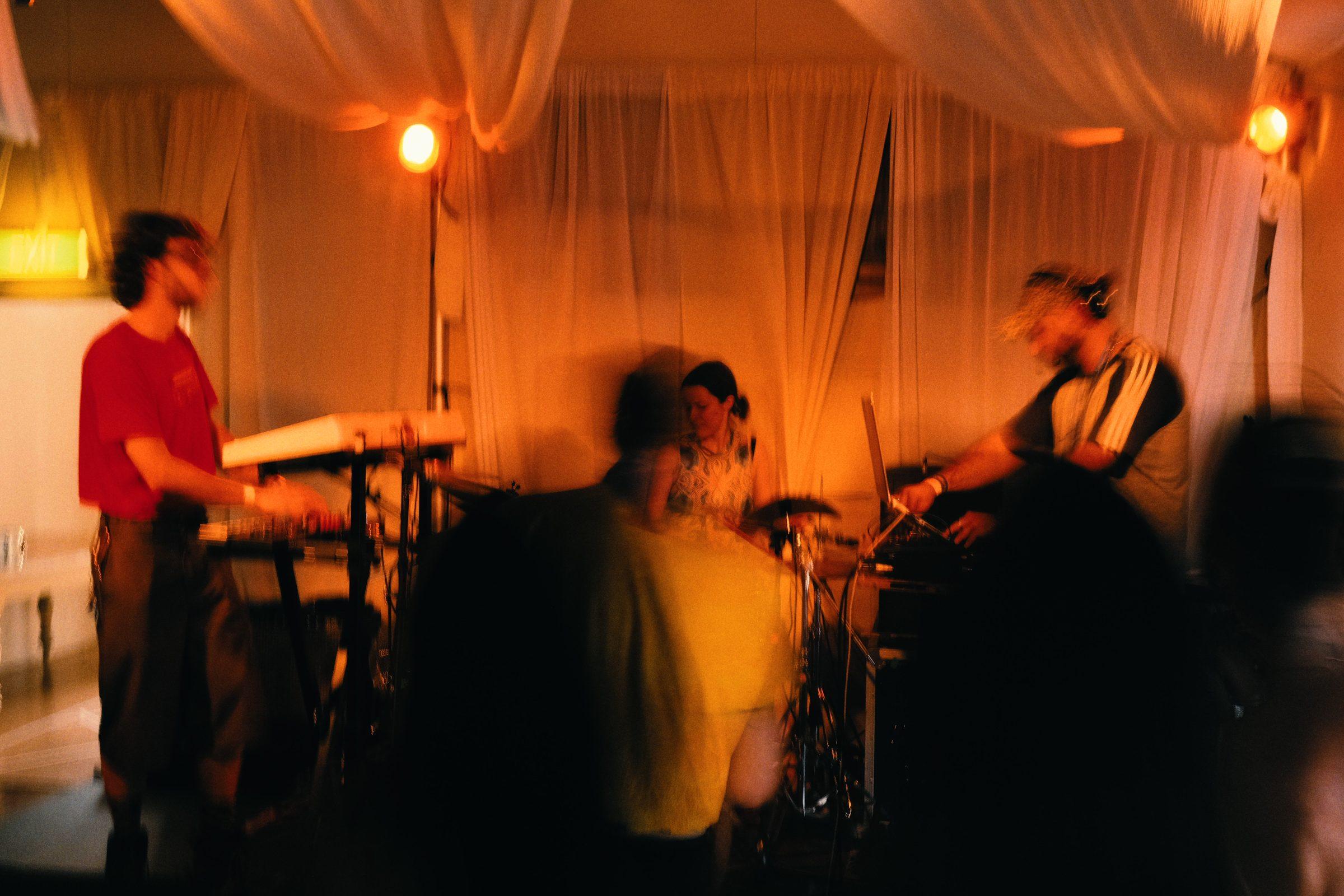 A band playing under draped white fabric and warm lights, in motion blur