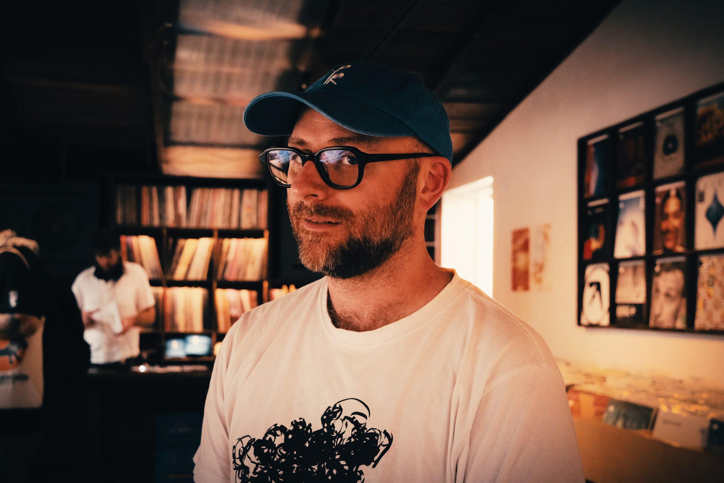A man in a white t-shirt standing in front of shelves of records