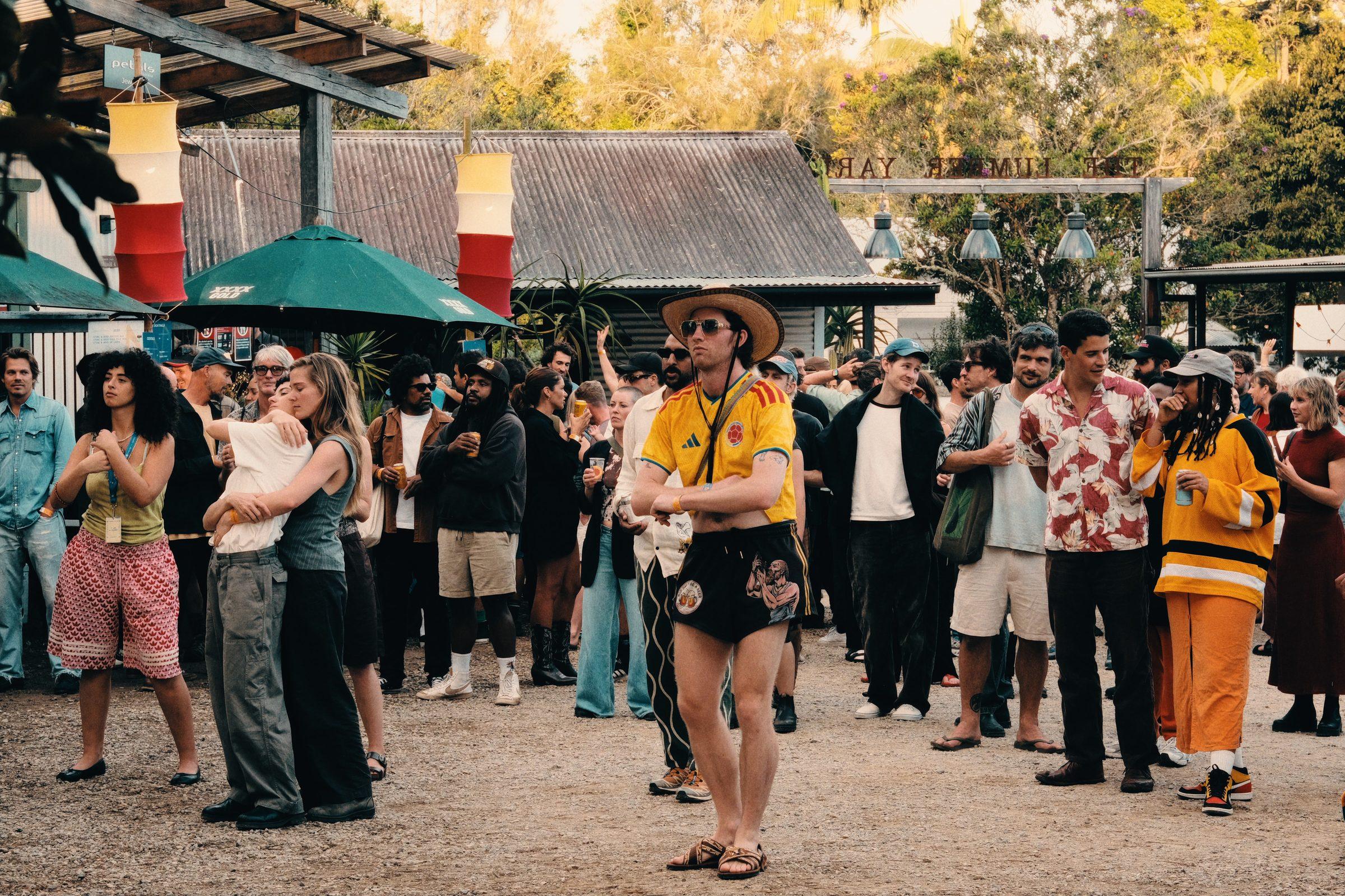 A crowd gathered in a yard in the late afternoon, a man in a yellow shirt in the middle