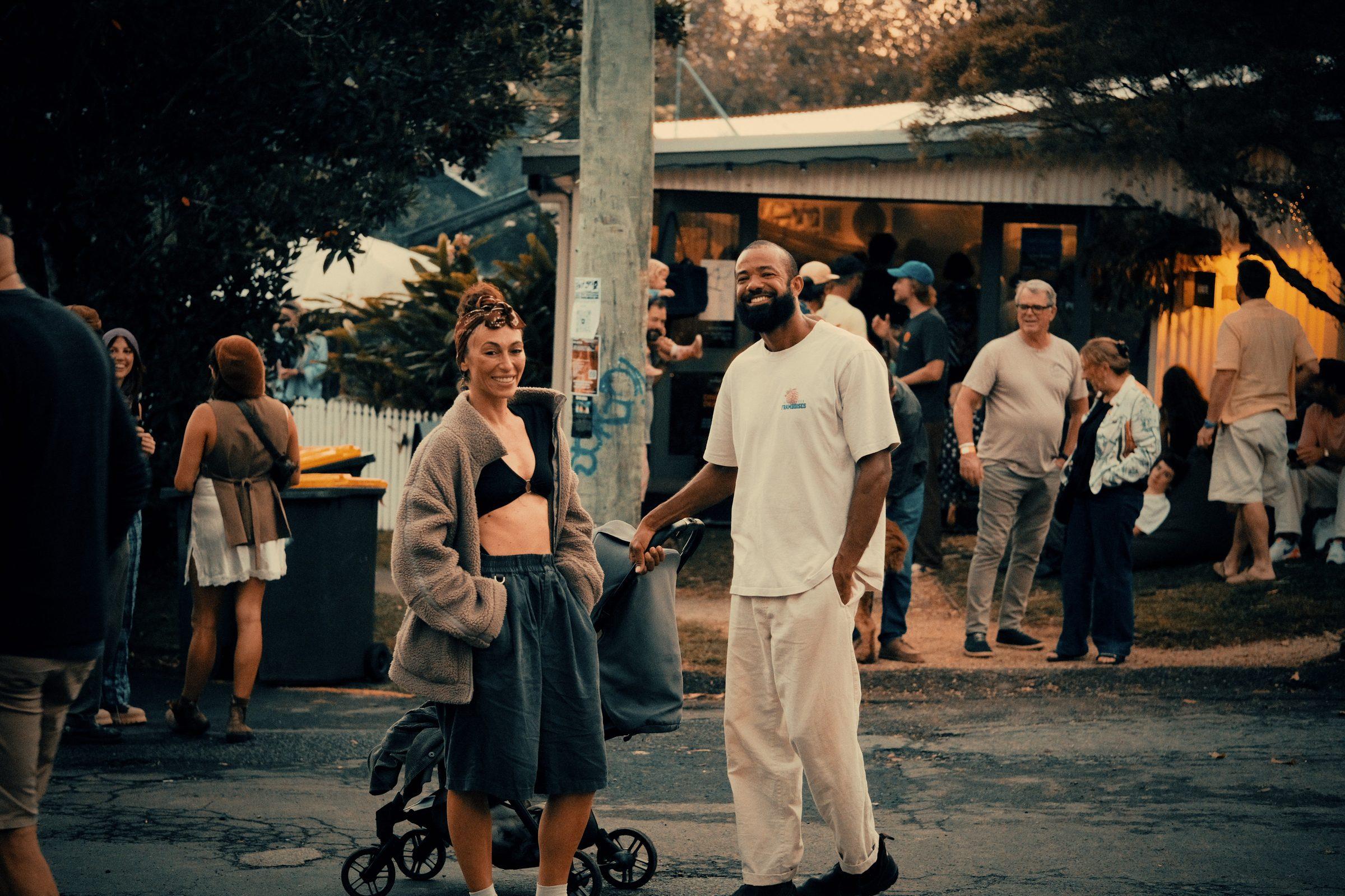 A man in white and a woman pushing a pram, walking down a street
